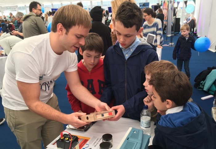 4 boys with researcher showing demonstration on SPIN-Lab stall