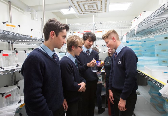 Four boys in school uniform standing in a lab looking at a small plastic sphere