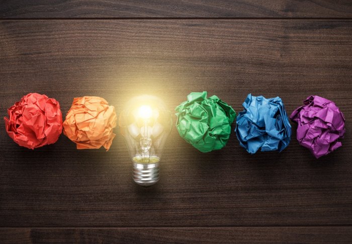 Five colourful scrunched up pieces of paper in a row, with a lightbulb in the middle