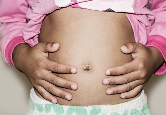 Hungry child with hands on belly, maybe with tummy pains. Close up of belly.