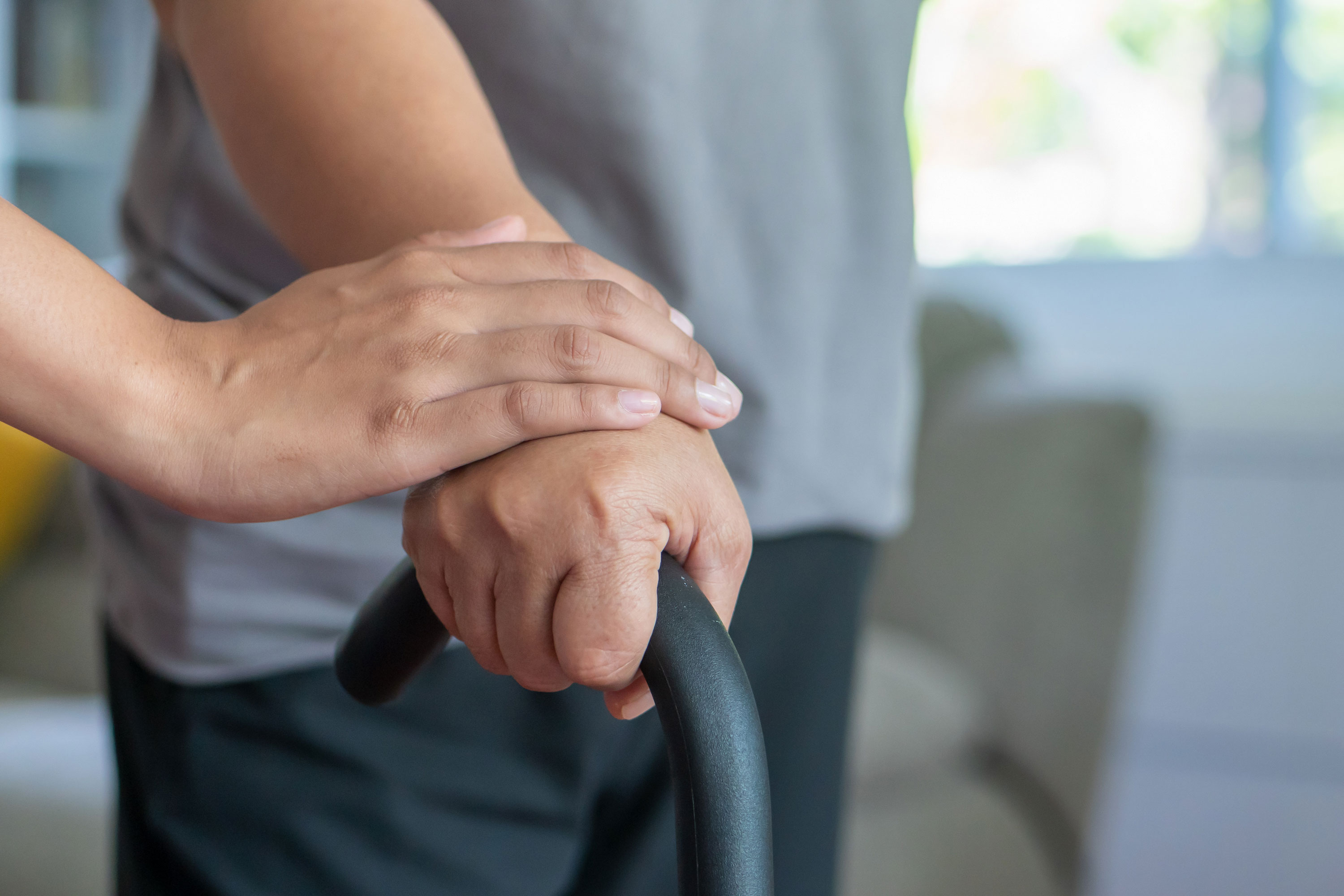 senior woman with walking disability using cane as walking aid, with helping hand of care giver or nurse
