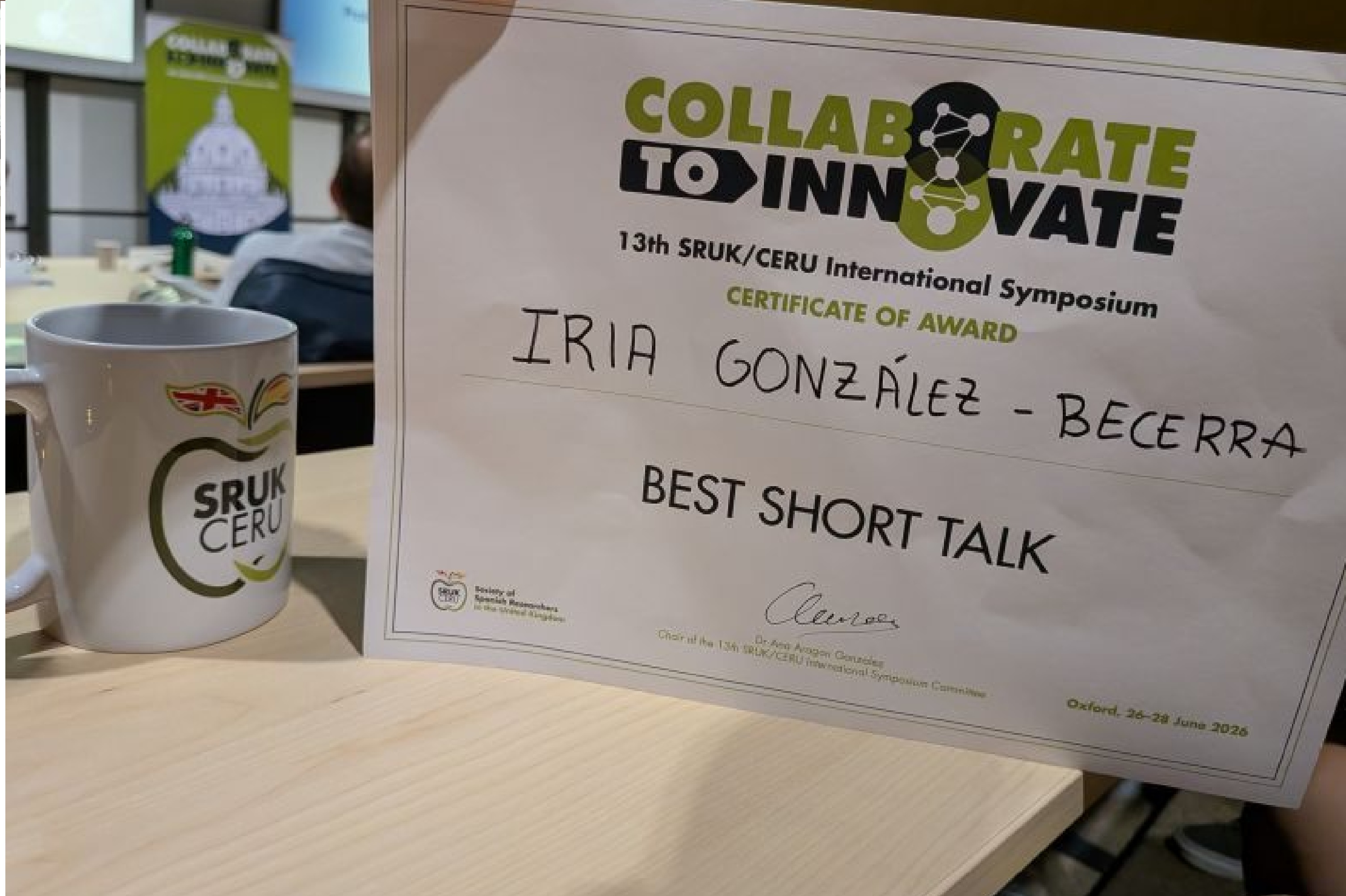 A certificate for 'Best Short Talk' awarded to Dr Iria Gonzalez Becerra, on a desk.