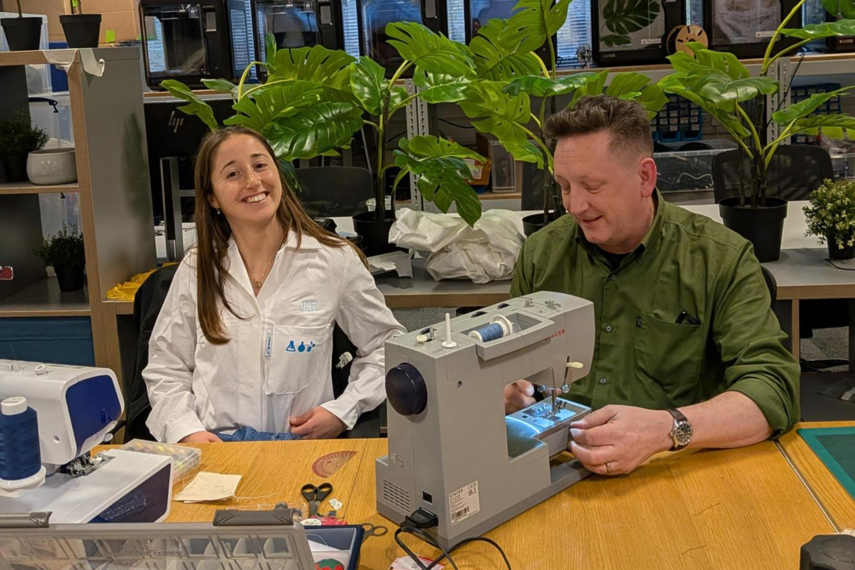 Student wearing a lab coat with embroidery and vinyl on, being shown how to use a sewing machine
