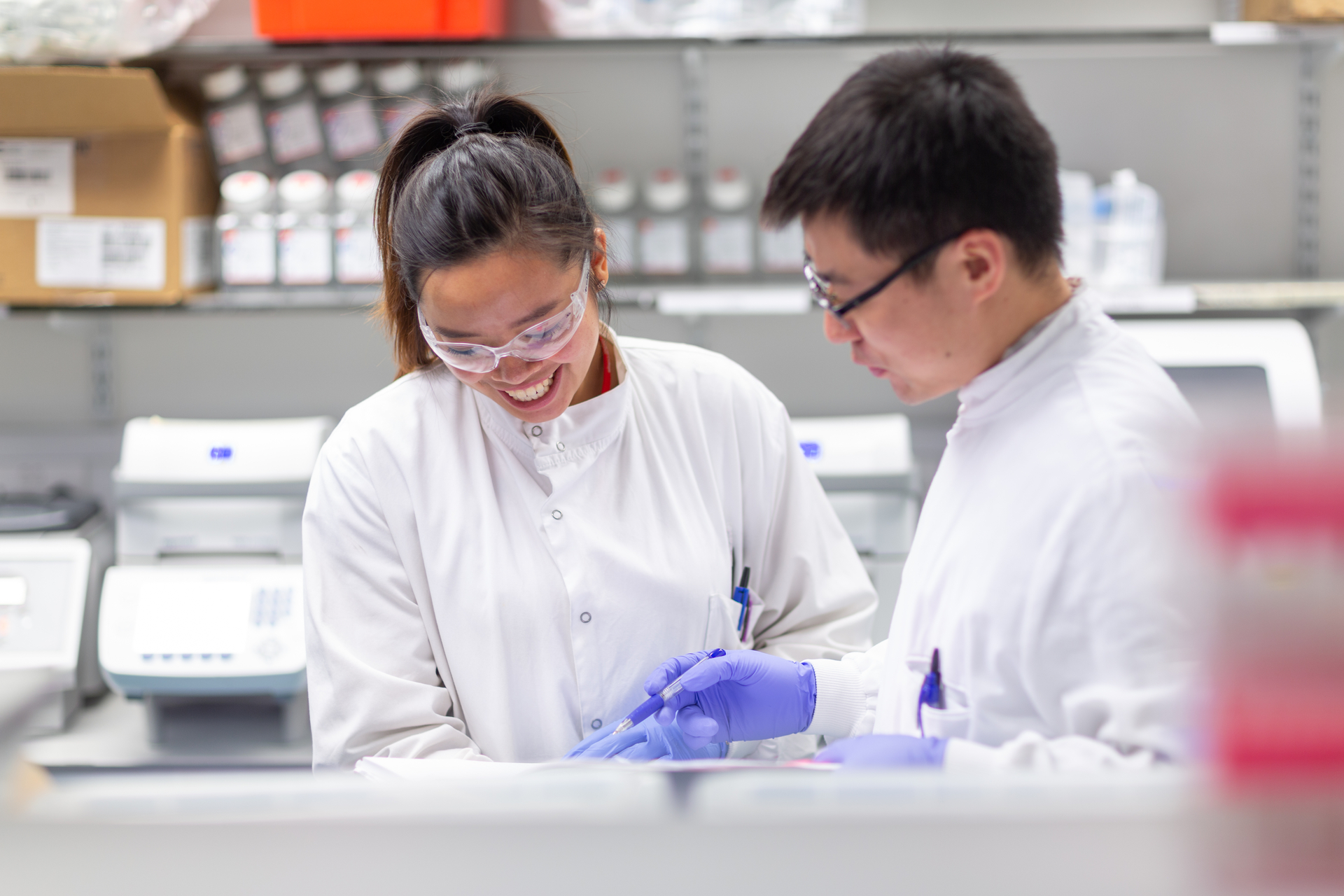 Two people in lab coats reviewing a document in a lab