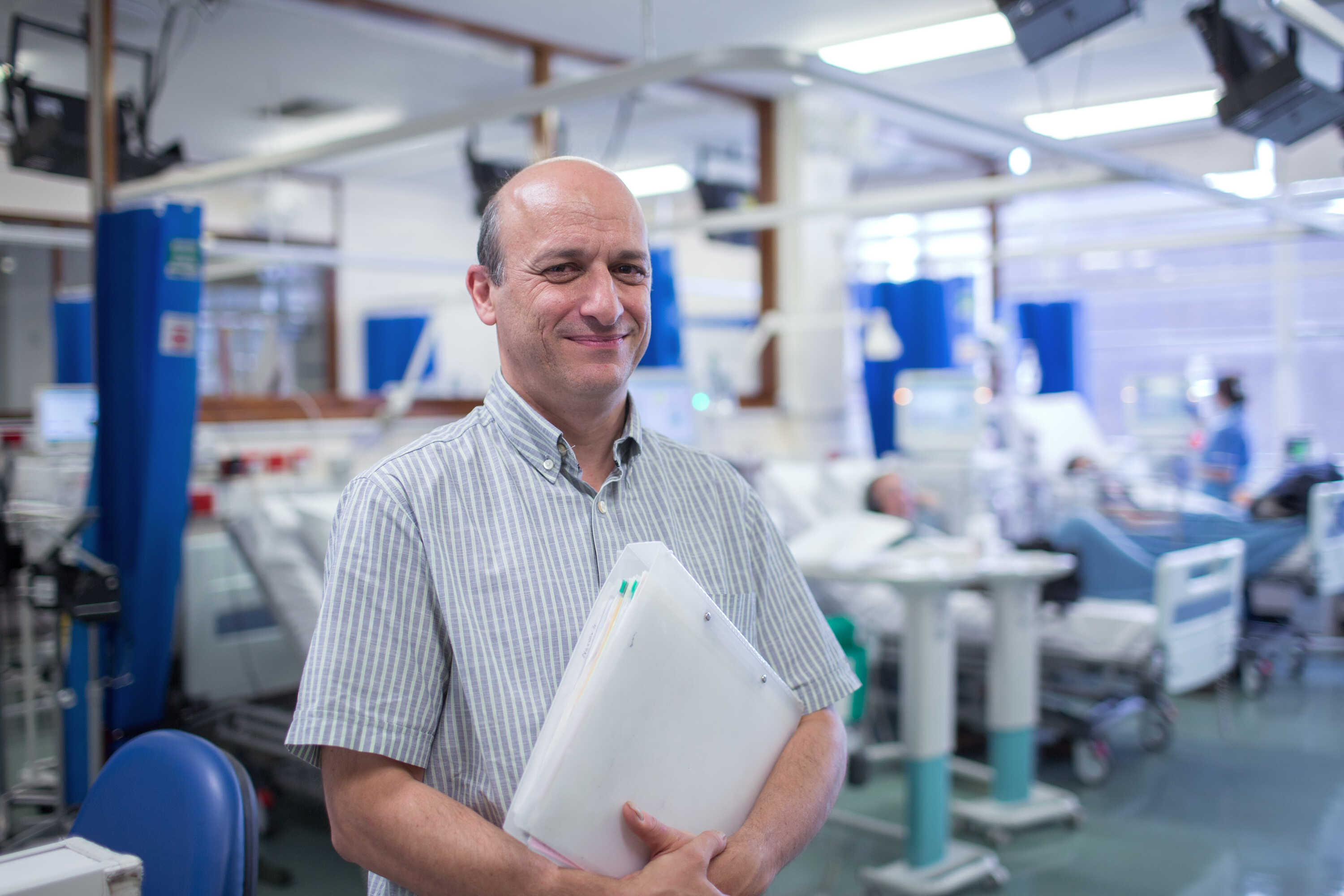 Professor Jeremy Levy standing inside a hospital ward with a folder in his hand