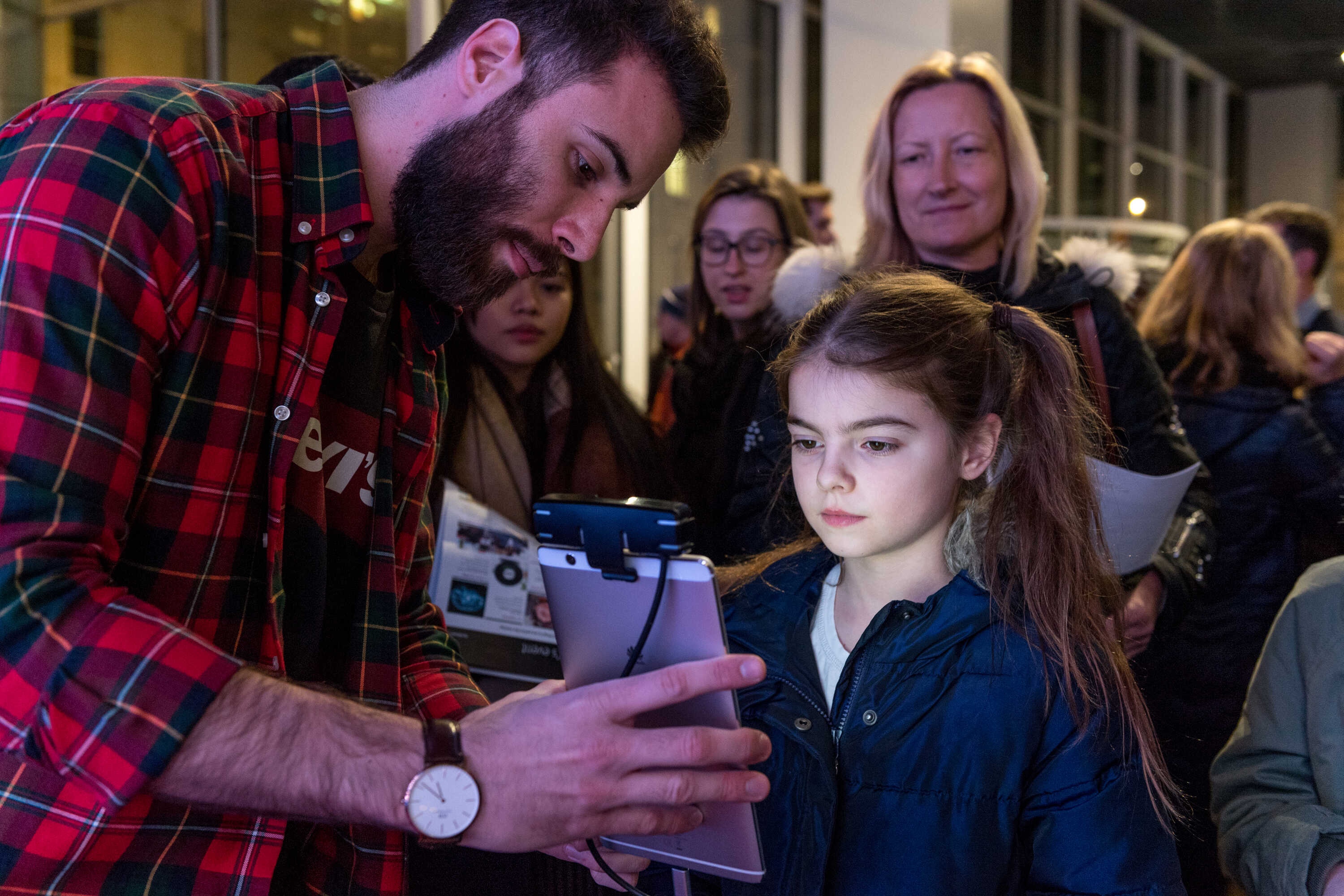 A young girl looks at a 3D face scanner held by a man with a beard
