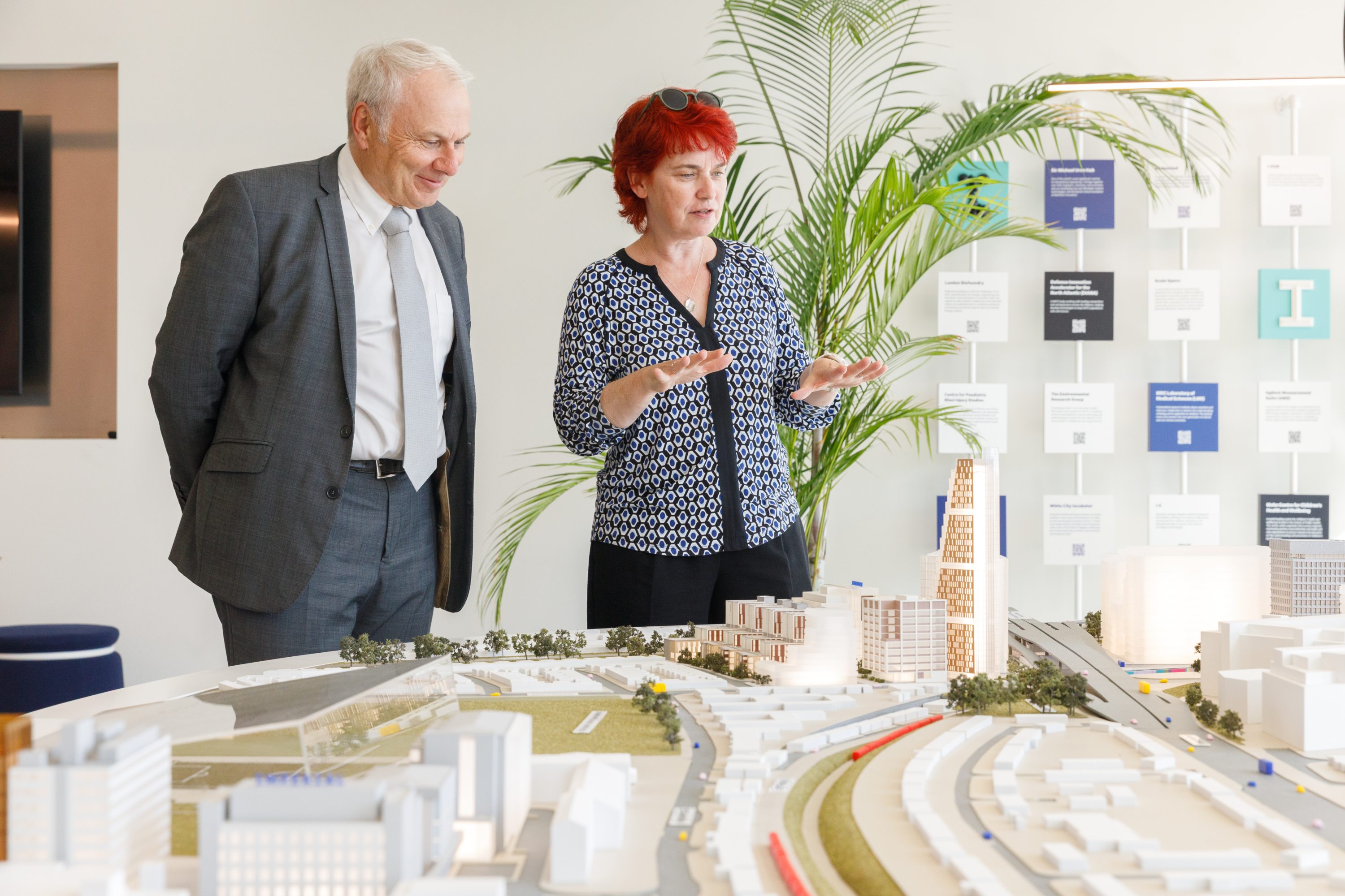 a man in a suit and a woman stand over an architectural model
