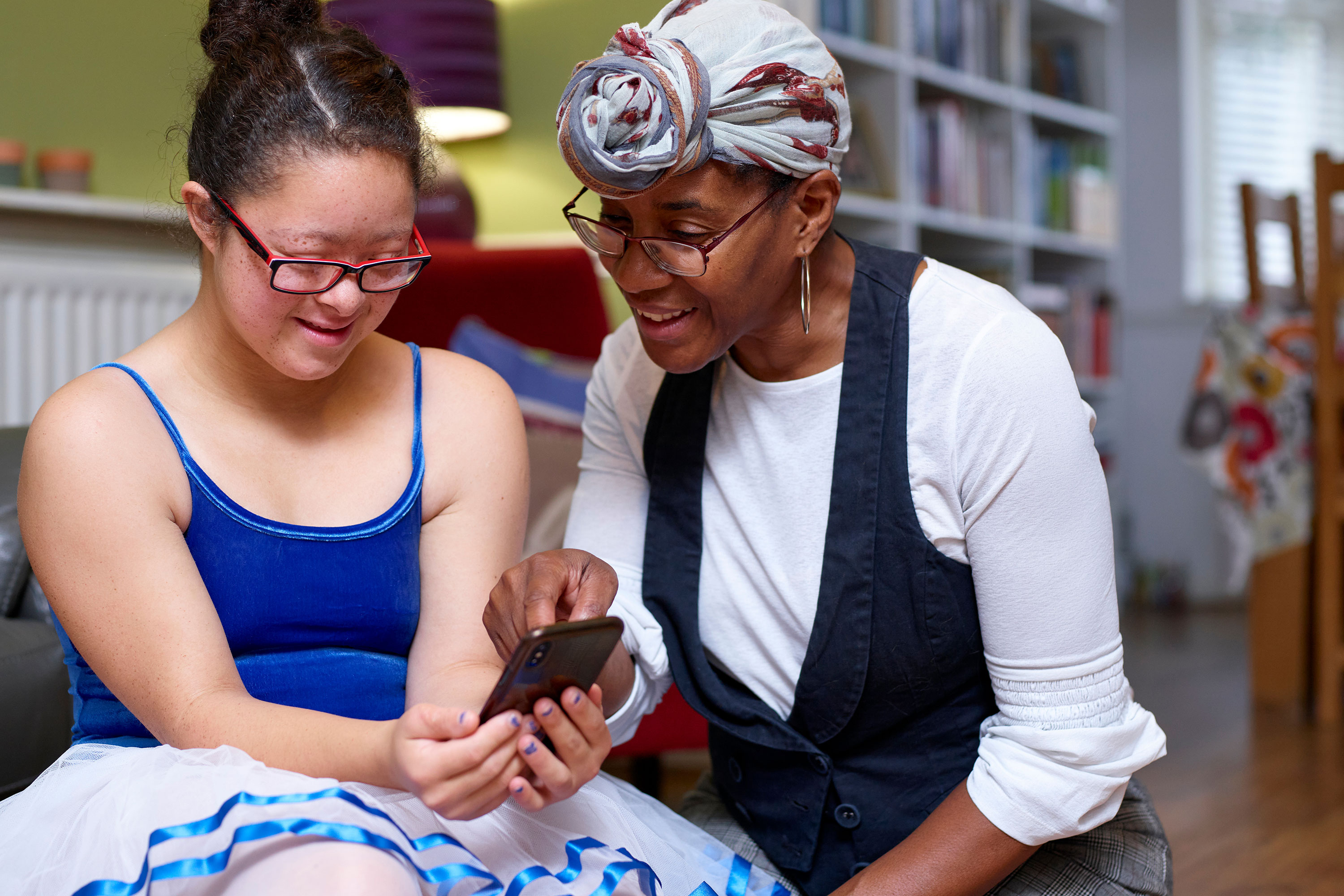 A person presents something on a smartphone to a girl with Down syndrome
