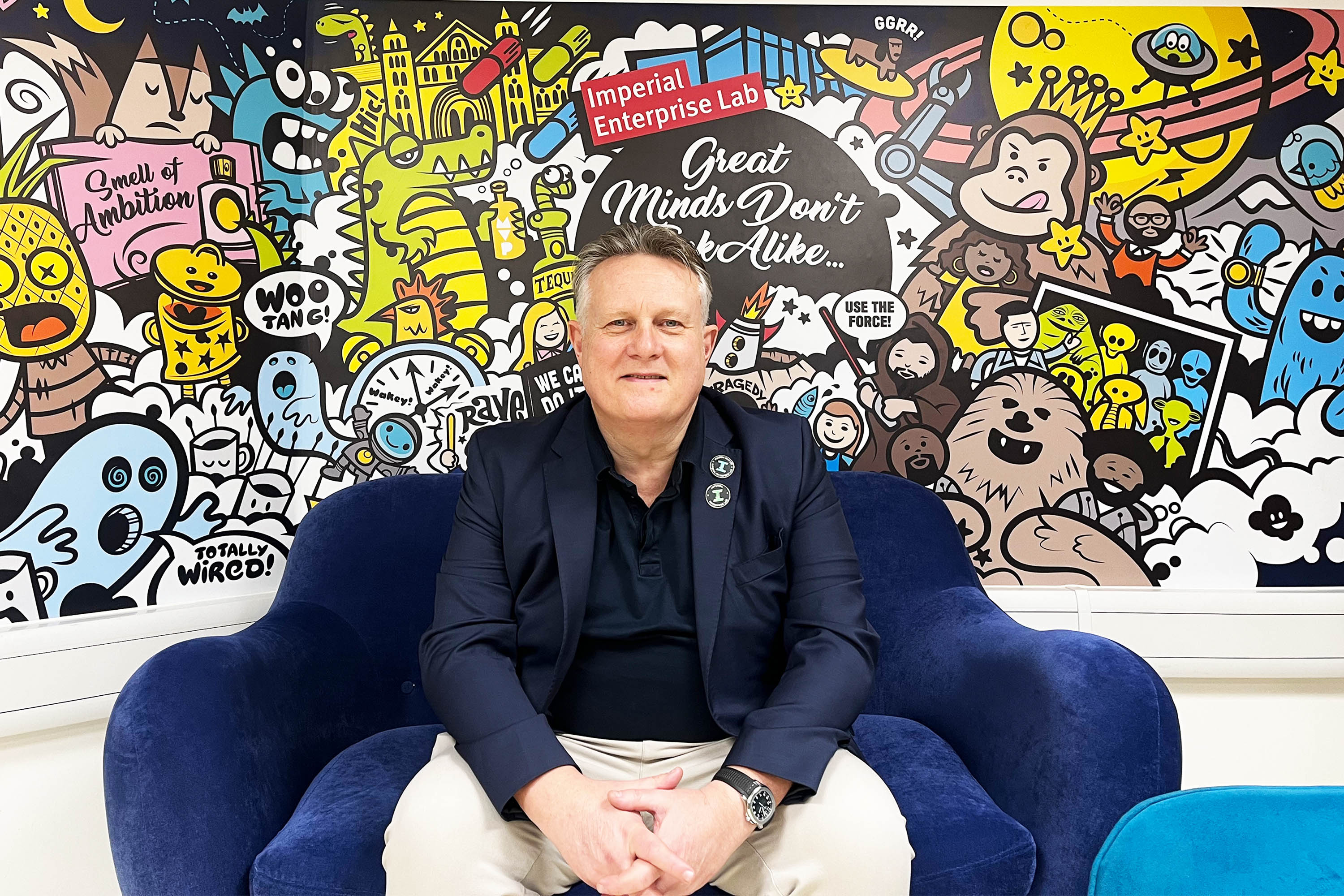 Martin Ward, entrepreneur-in-residence, sitting in a large blue chair at Imperial Enterprise Lab in front of a cartoon mural