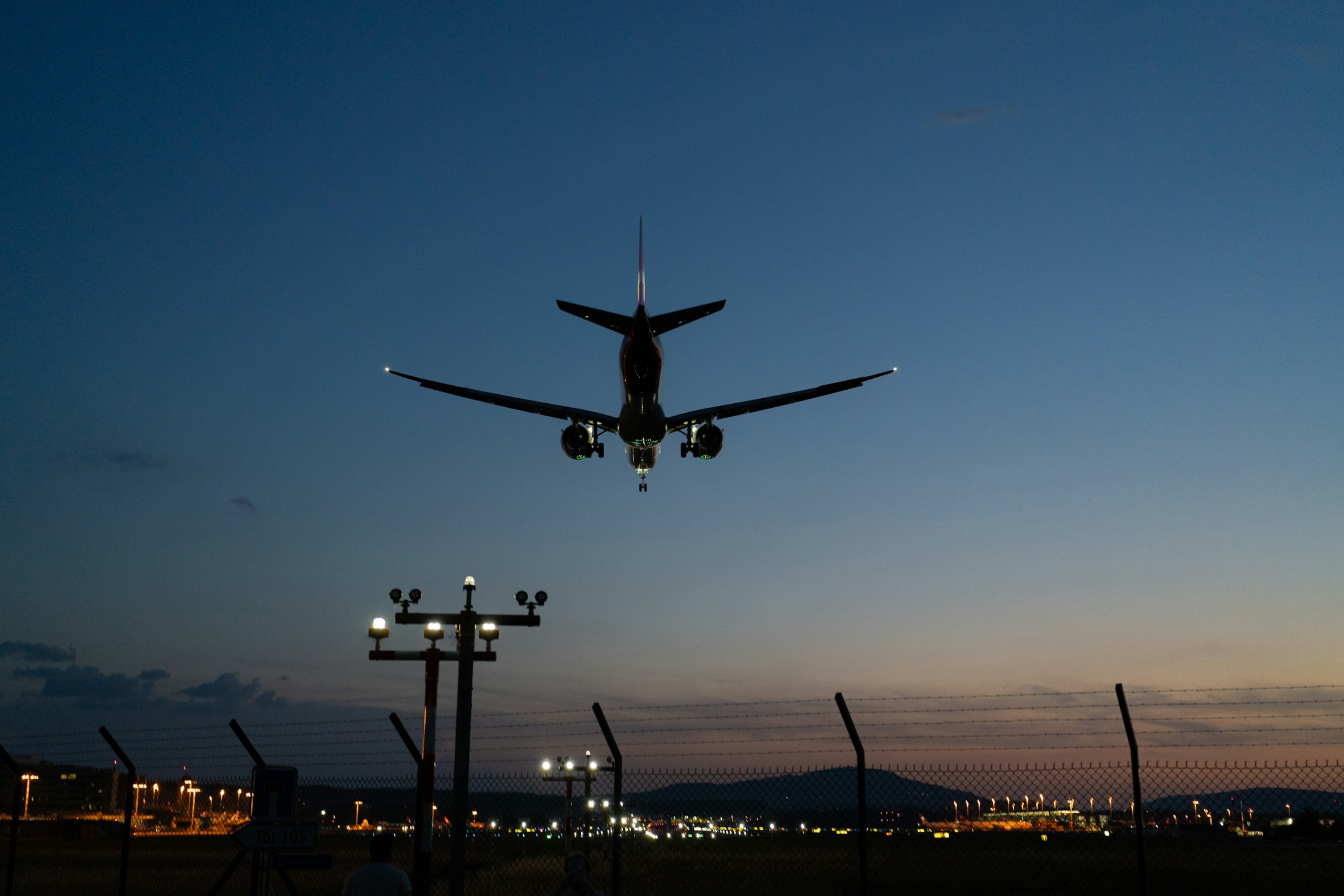 An airplane flying low over an airport at dusk