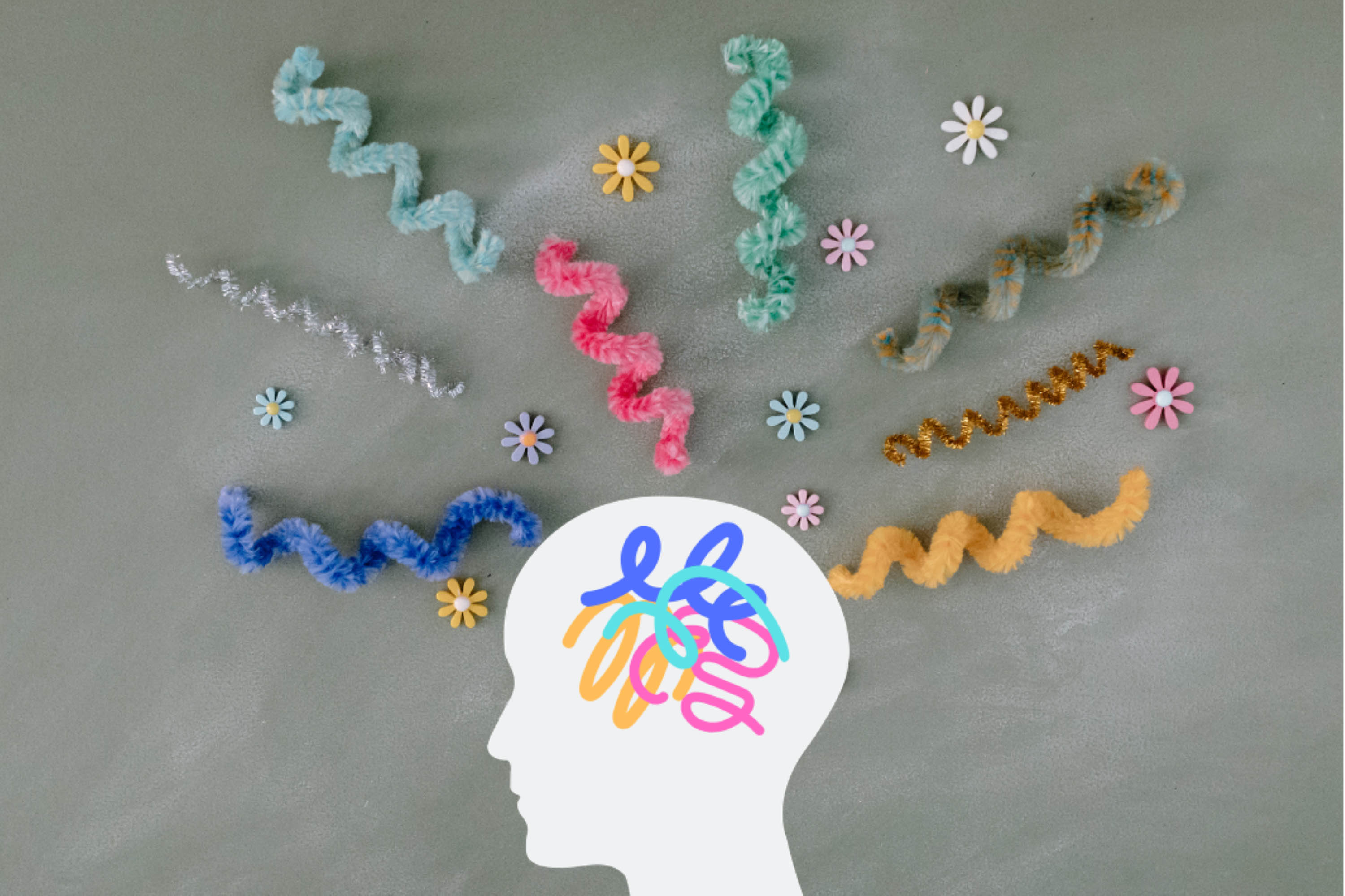 A silhouette of a head with colourful overlapping scribble-like shapes inside and around the head are brightly coloured pipe‑cleaner spirals and small decorative flowers.