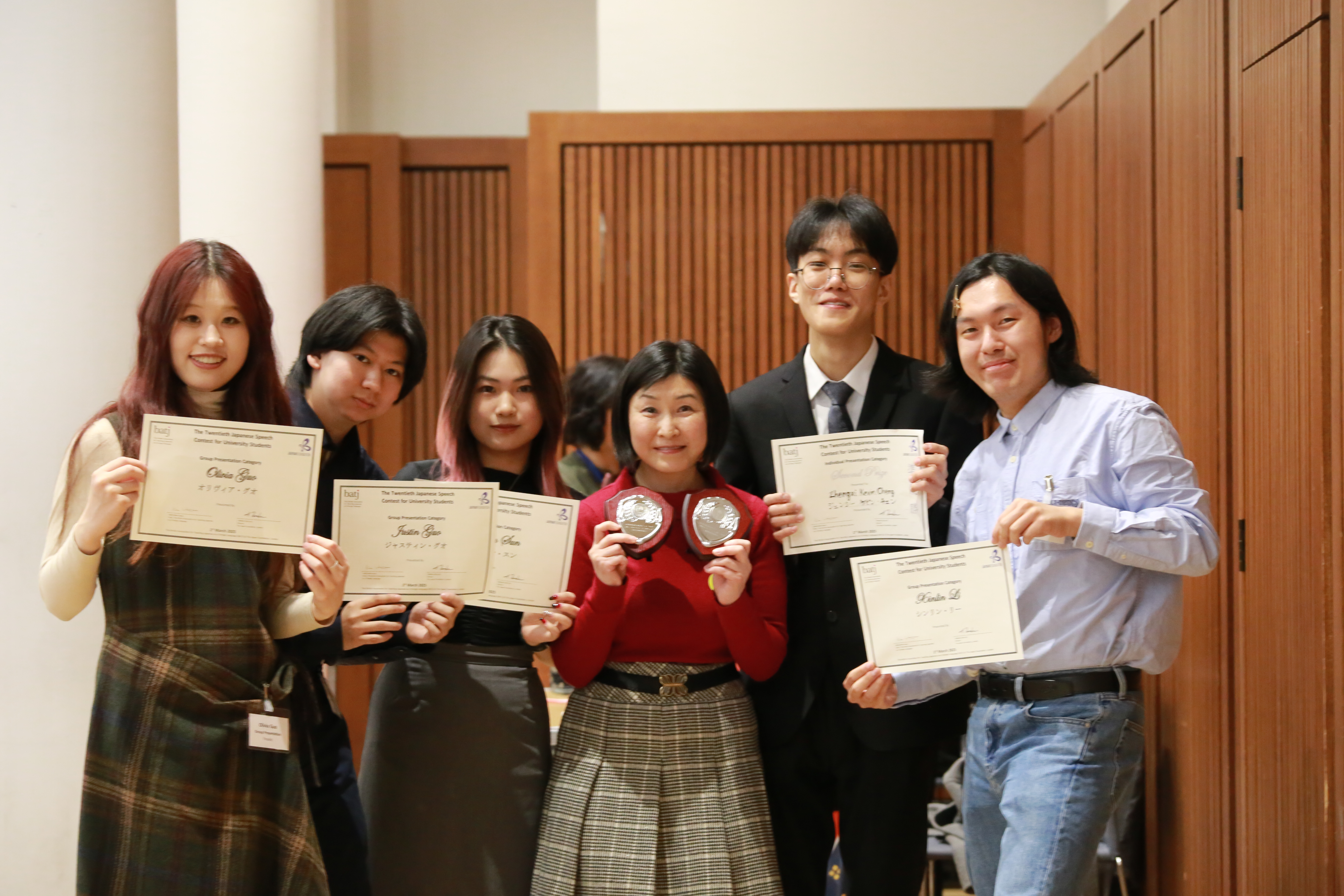 5 students with certificates and teacher with 2 plaques or medals