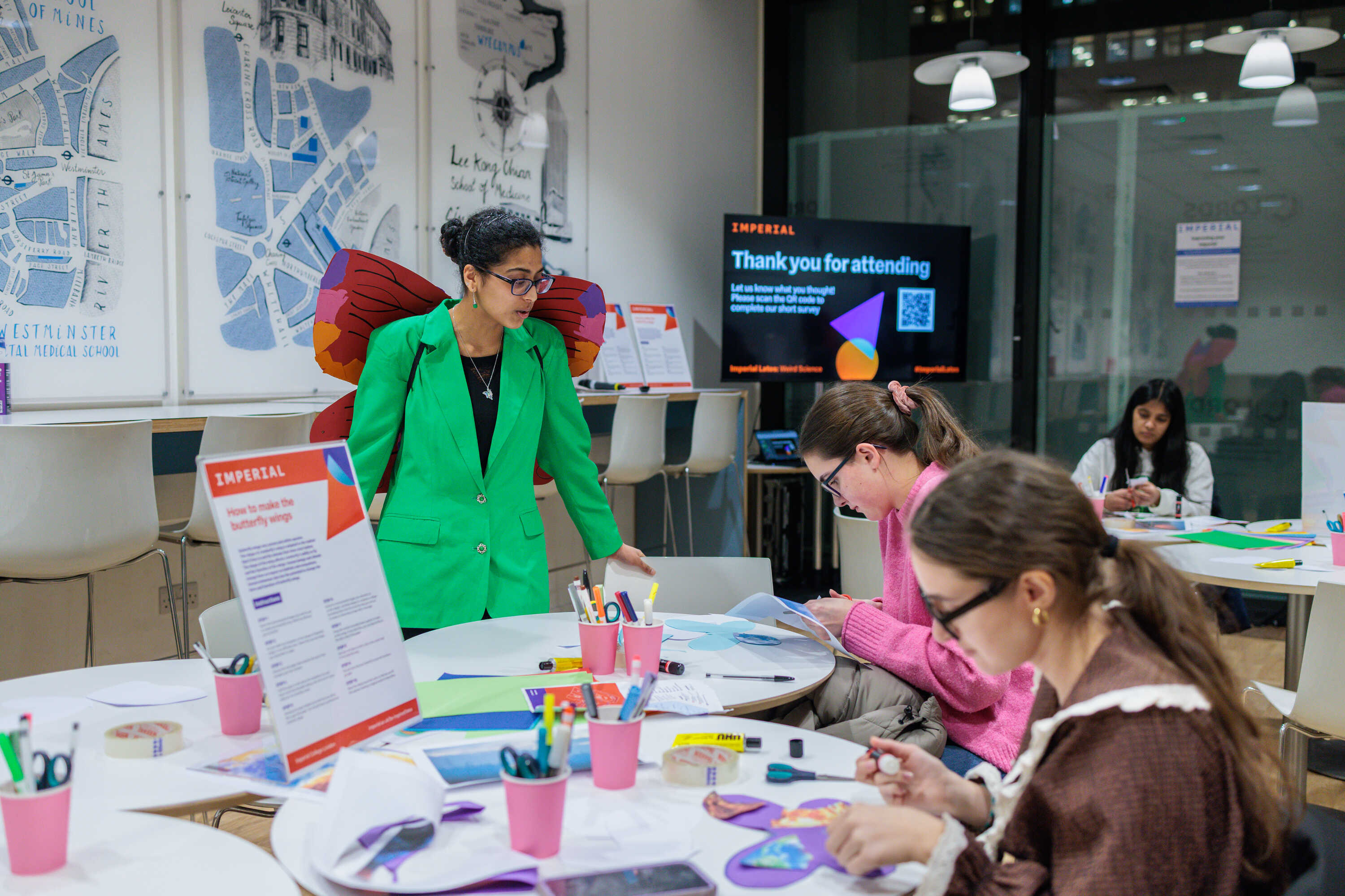 Mahika standing next to two girls sitting at a table constructing butterfly wings