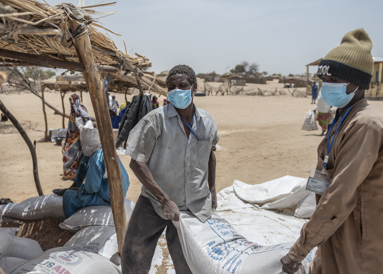 Bags of food labeled USAID WFP are handed out by two men wearing surgical masks