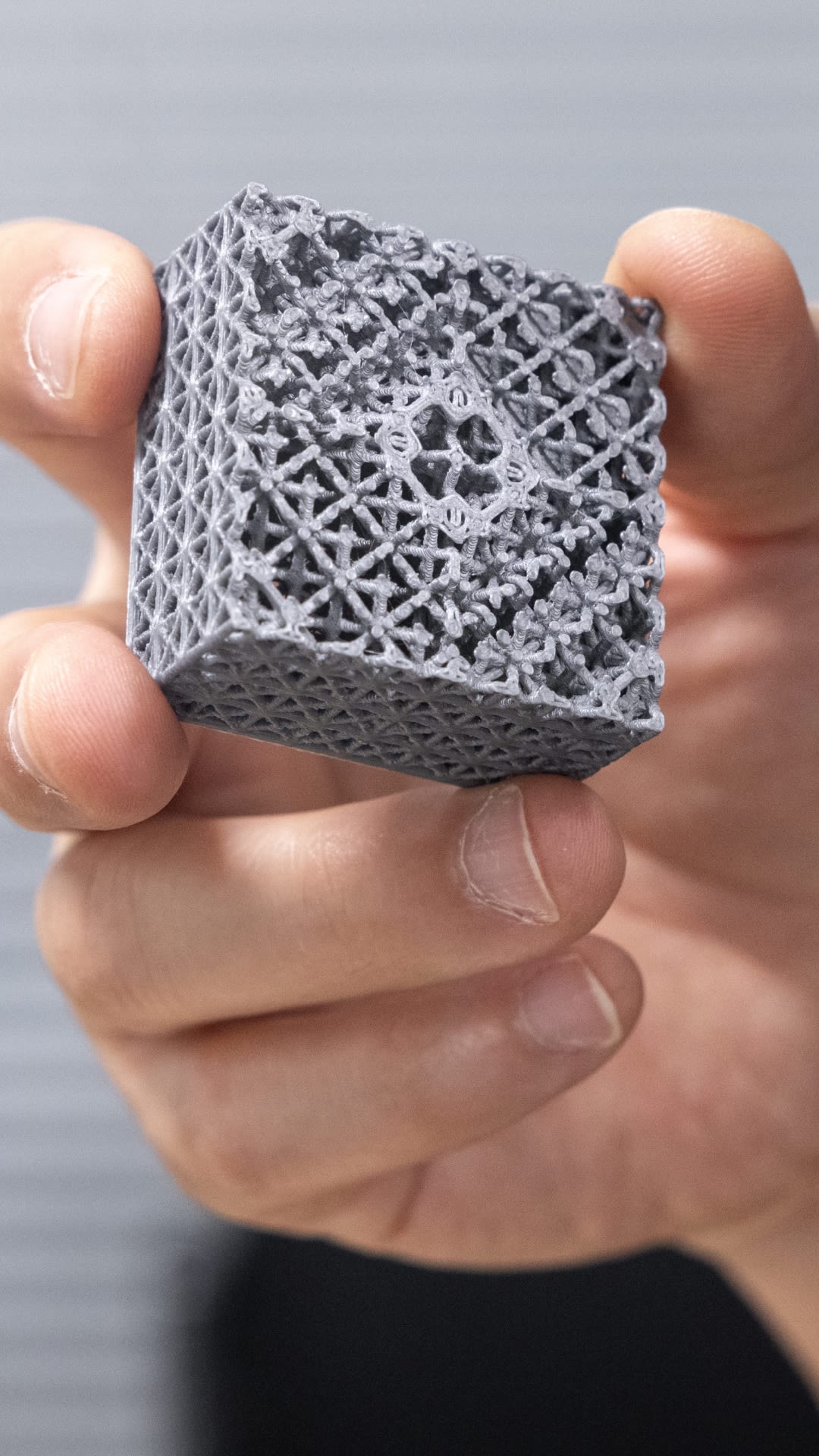 Dr Minh-Son Pham holds a square 3D printed model, which has been cut in half to reveal the complexity of the lattice structure. This structure features a lattice structure of small diamonds, each containing a cross.