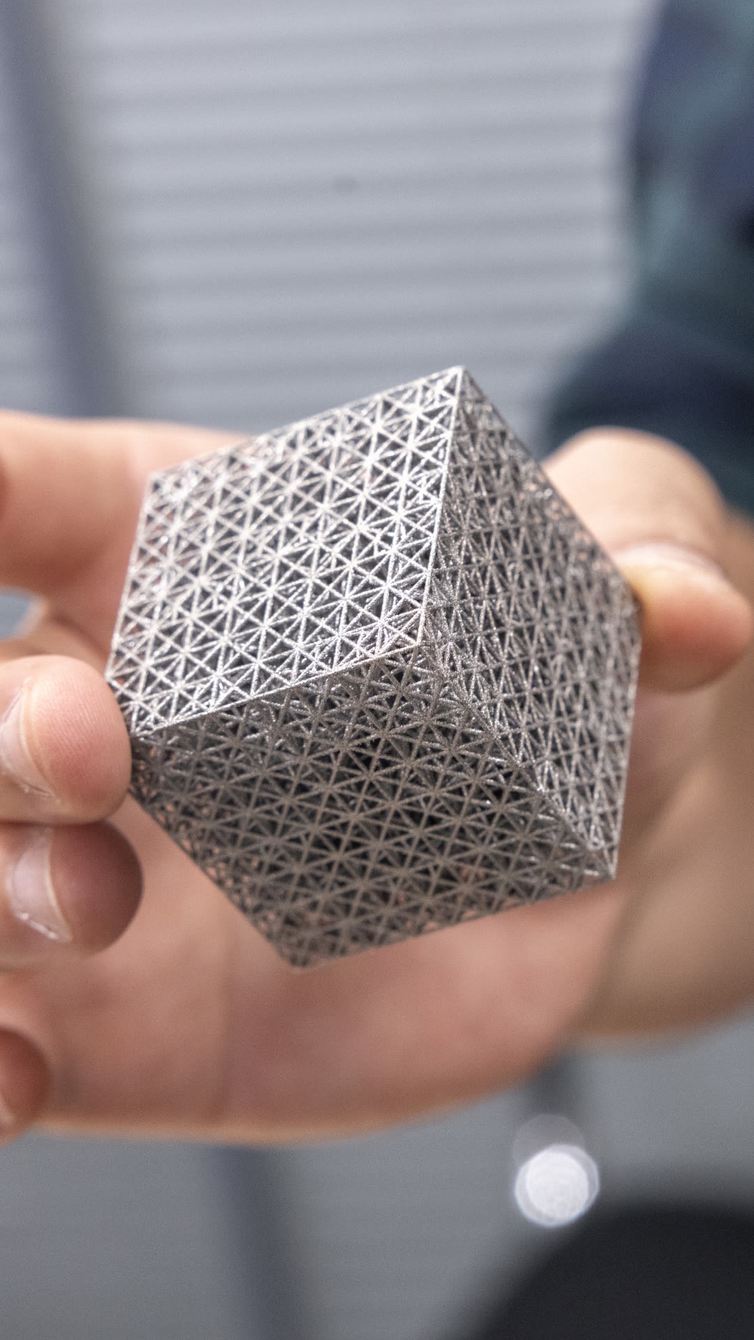 Dr Minh-Son Pham holds a square 3D printed model, with a complex lattice structure. This structure has many squares, each containing a cross.