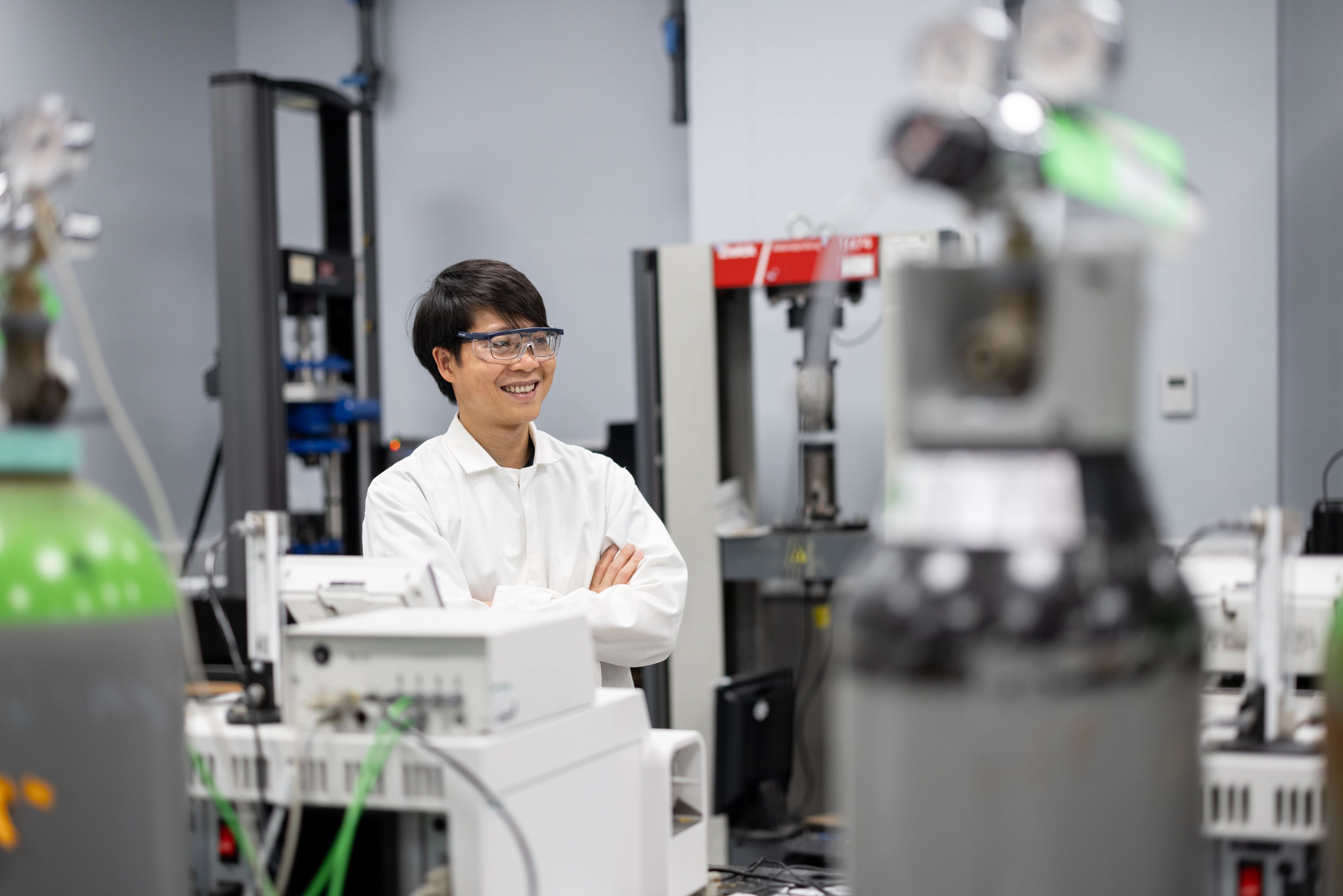 Dr Minh-Son Pham standing in the laboratory with his arms folded. He is smiling at a colleague who is off camera.