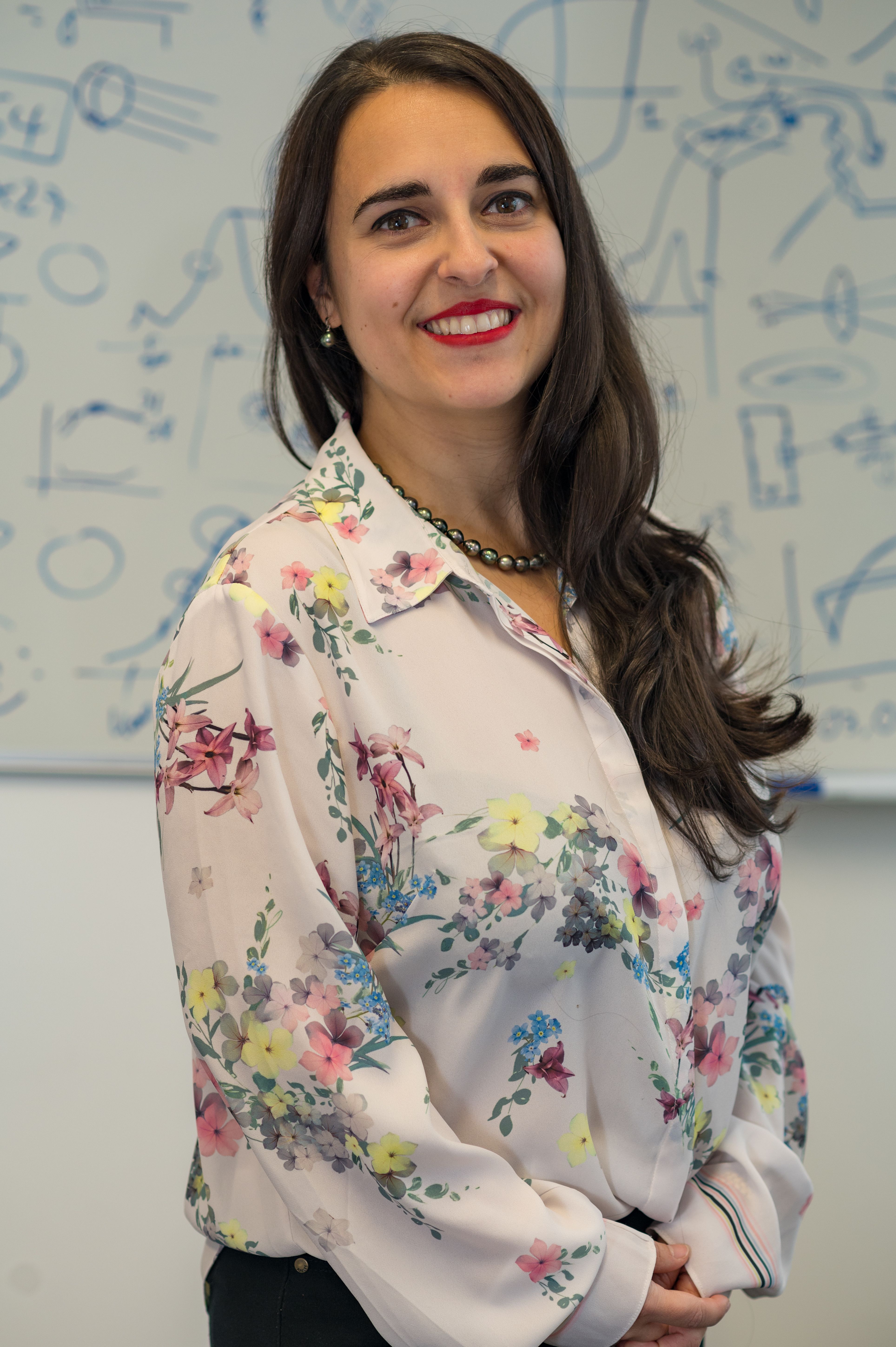 Portrait image of Giuliana standing in front of a whiteboard filled with working and symbols.