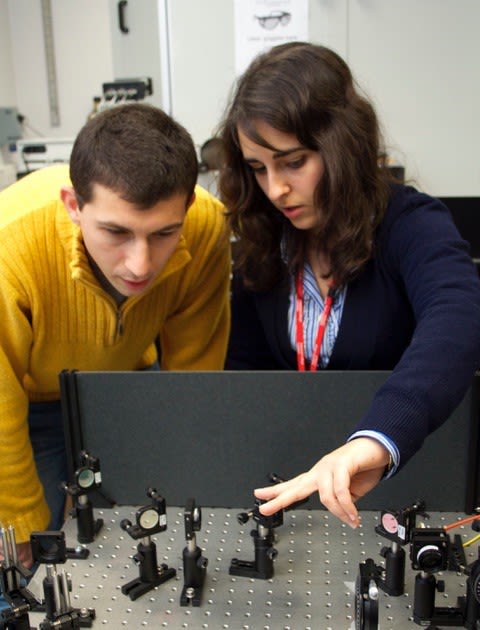Giuliana in a lab, she wears a lanyard around her neck and is with one colleague who is wearing a yellow shirt