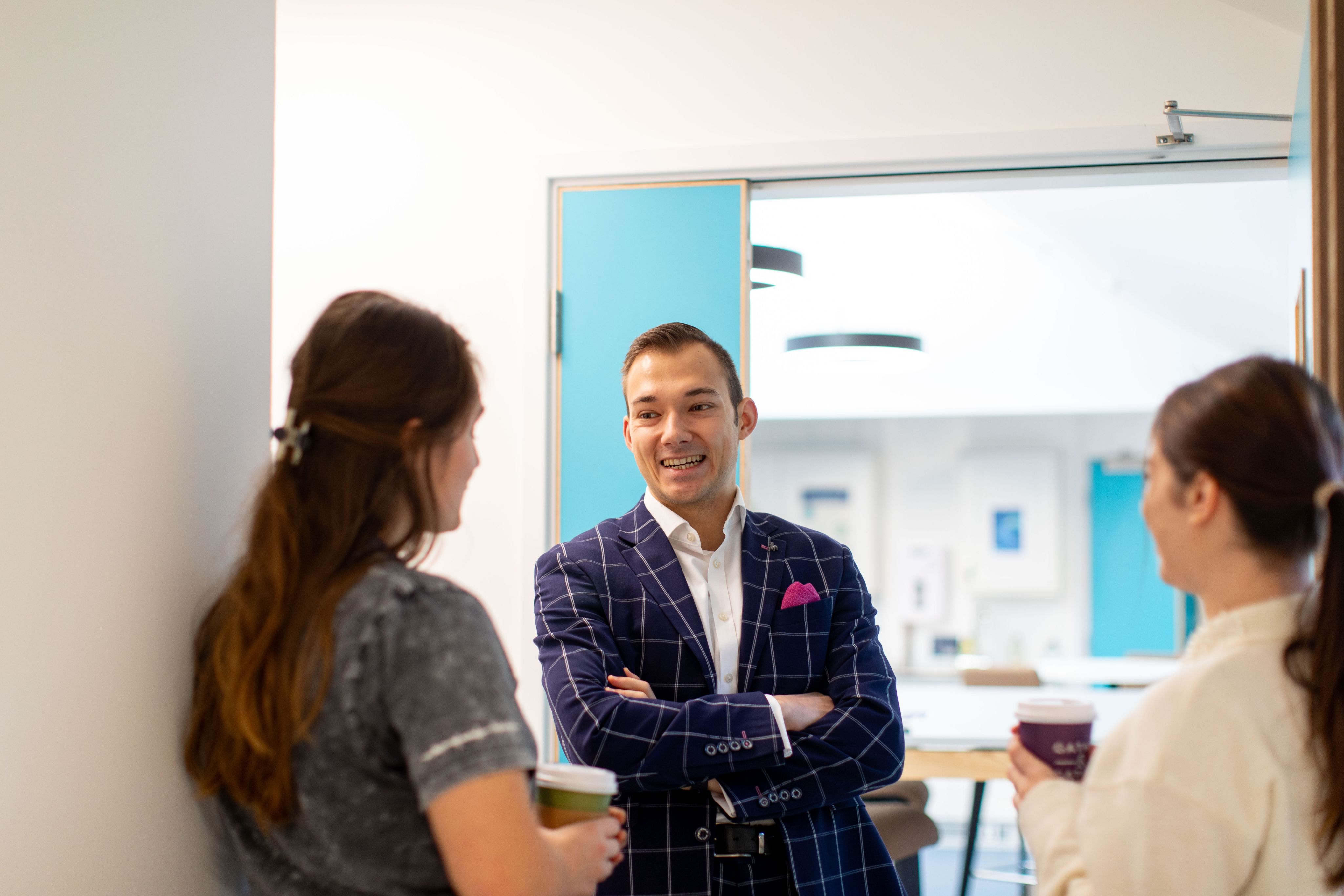 Miroslav smiling and chatting in a doorway with two female colleagues. He has his arms crossed against his chest 