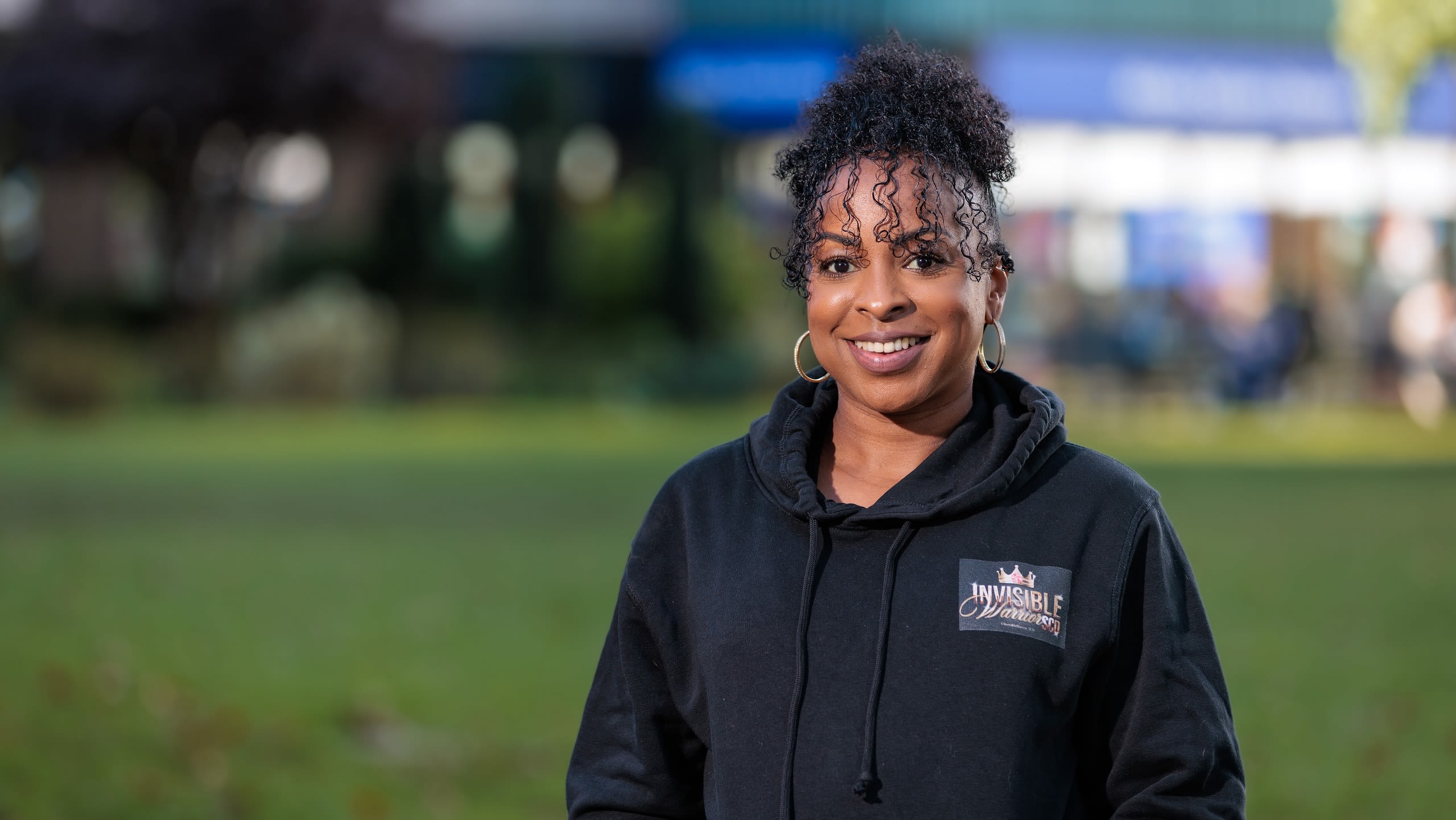 An image of Sickle Cell Warrior Louisa Thompson, smiling, wearing a hoddy with her hair tied up.