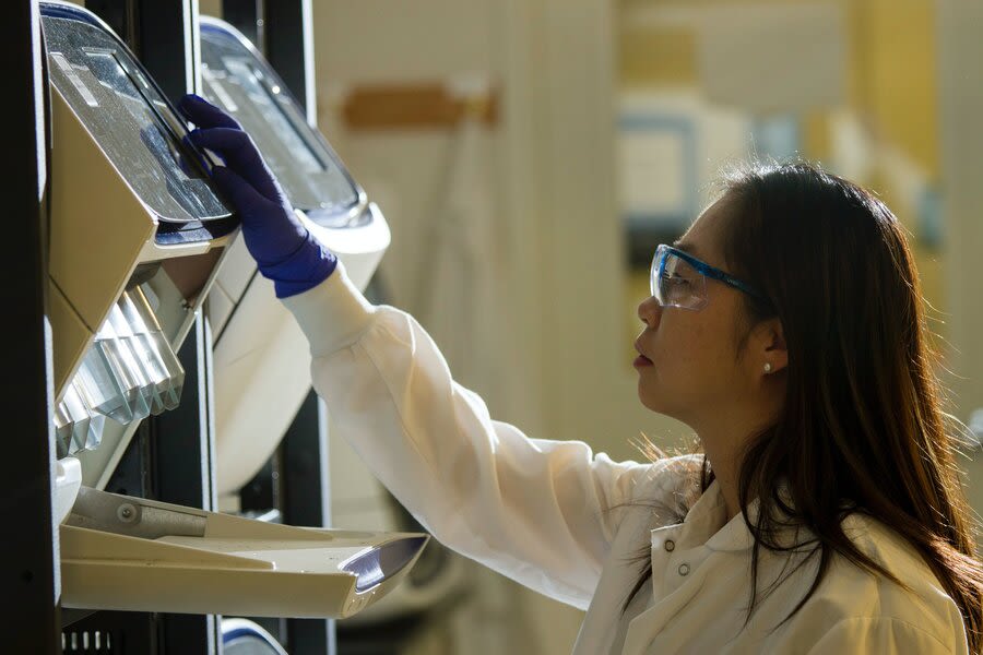 a person wearing blue gloves and white coat using equipment in a laboratory