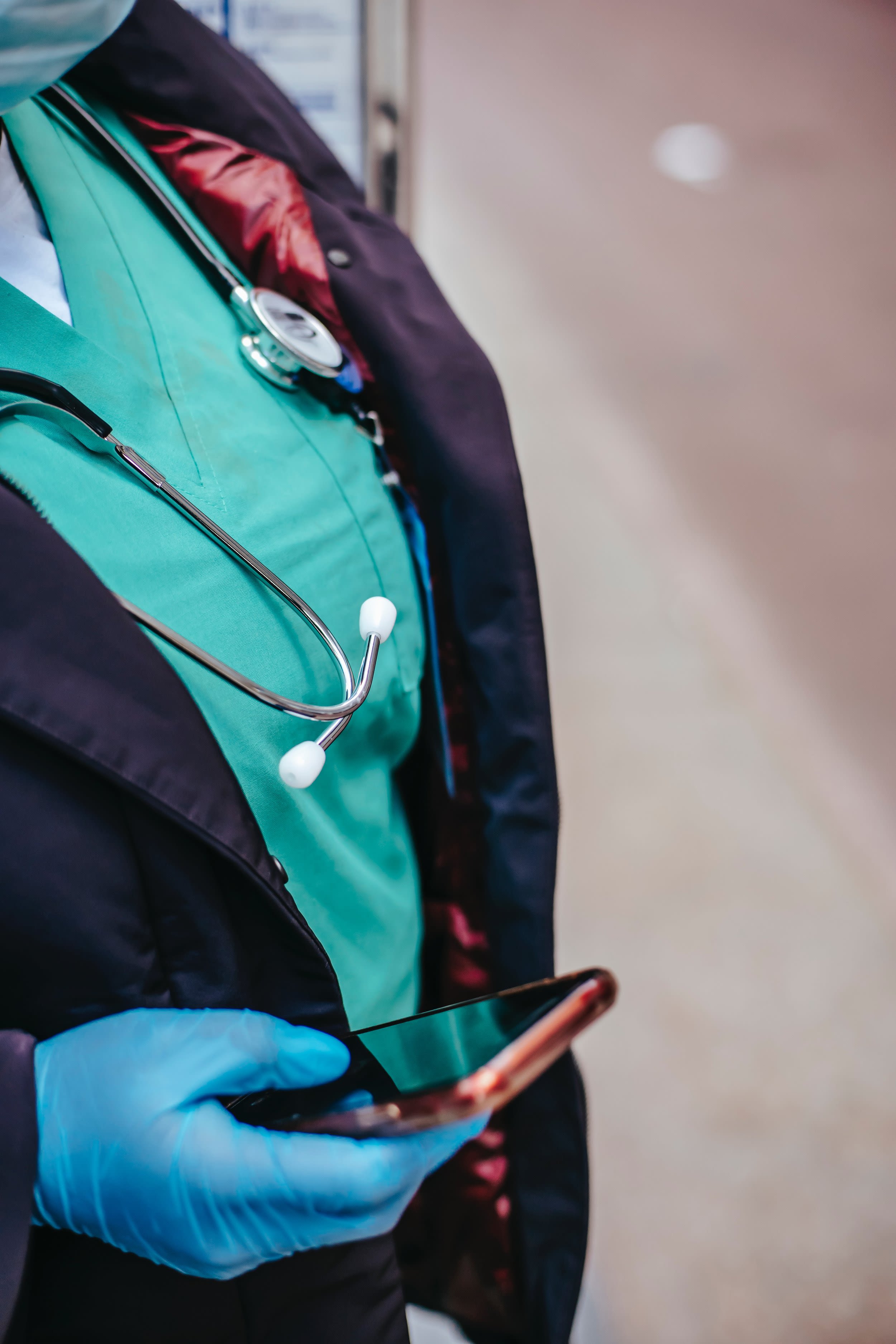 A close up of a doctor's gloved hand holding a mobile phone