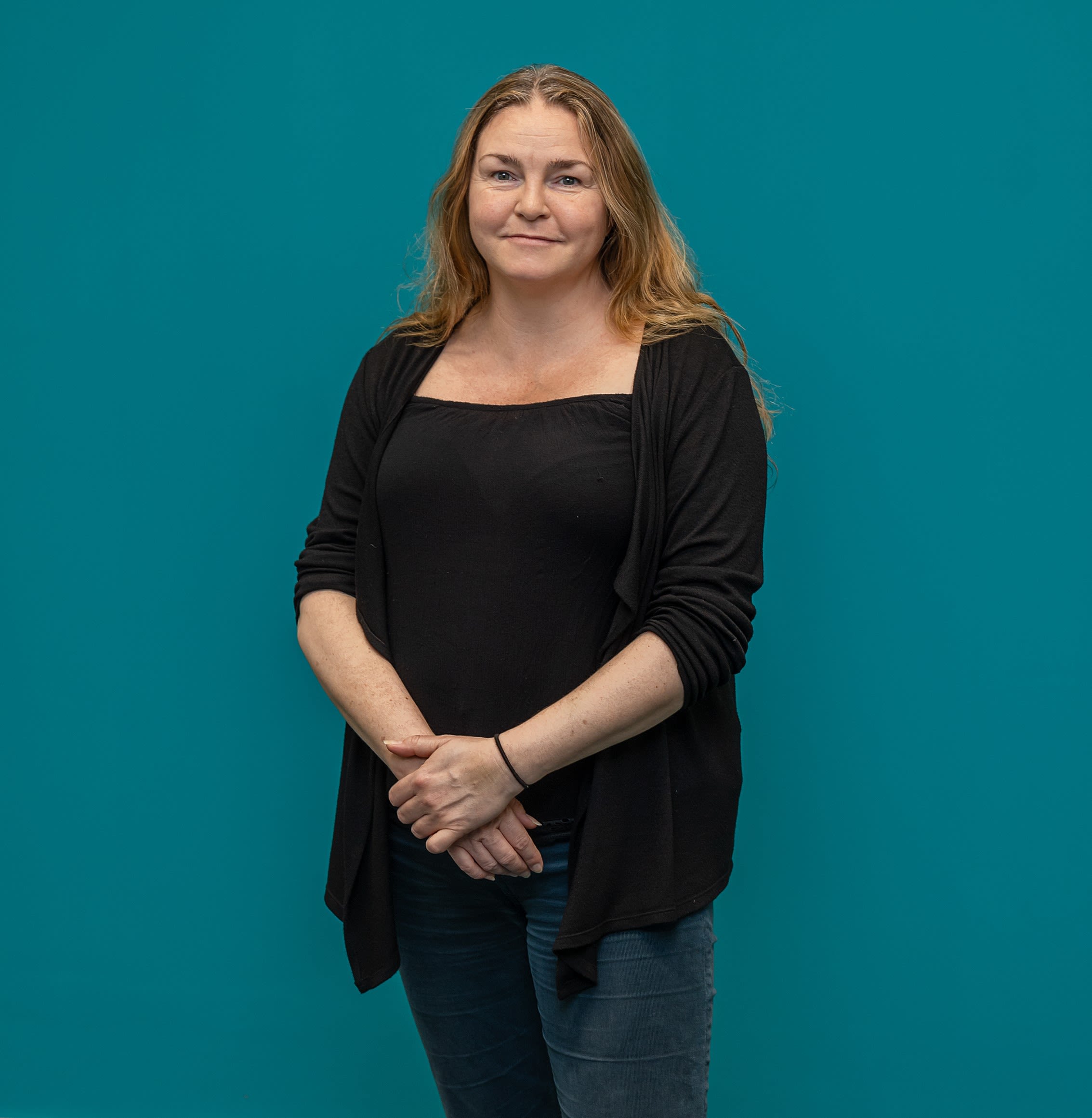Sam Tolhurst, dressed in black against a teal background, has long hai