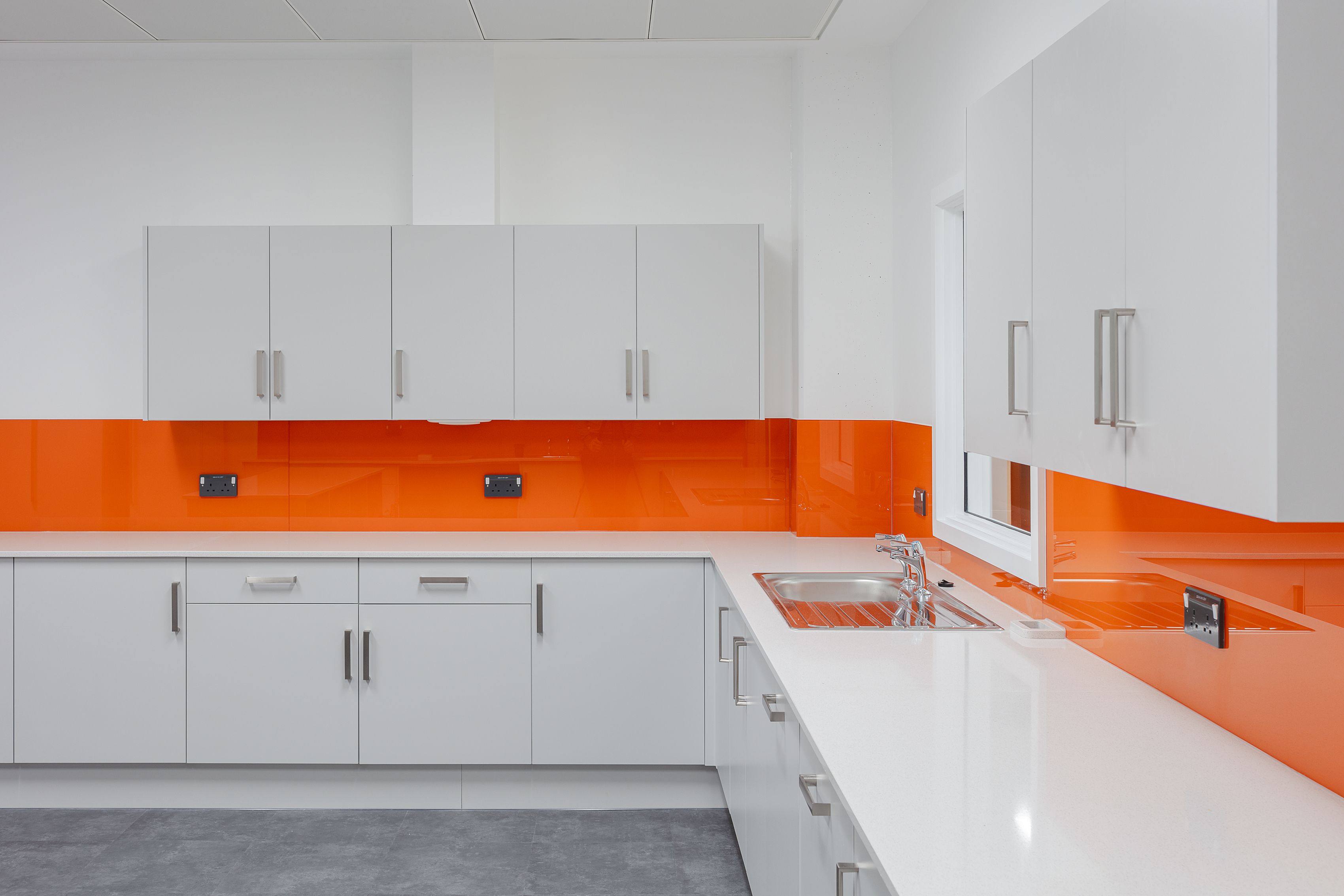 A close up of the communal kitchen area, with organge feature wall above the sink and worktops