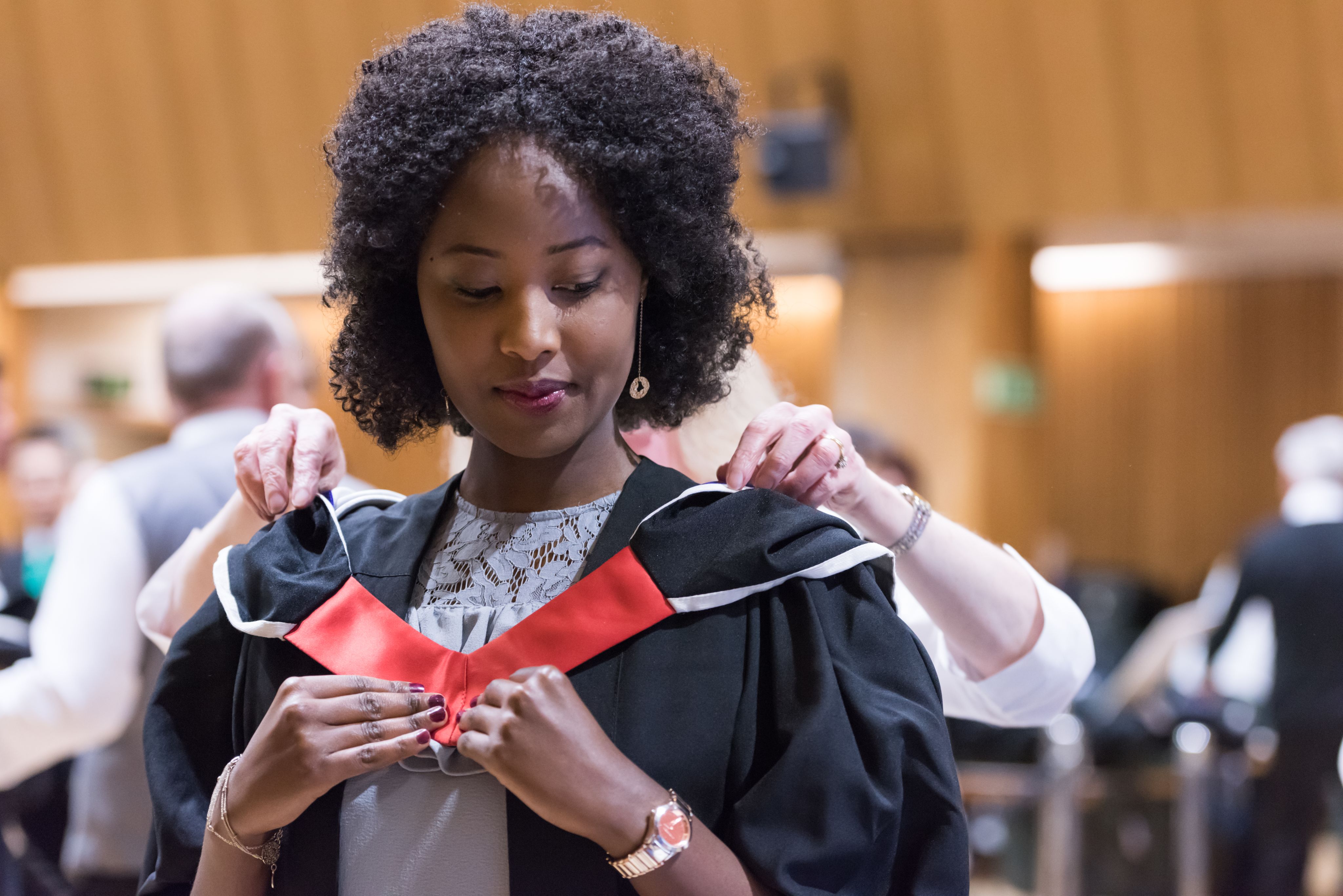 A black female graduand gets robed before her postgraduate graduation ceremony in the Great Hall, 2018.