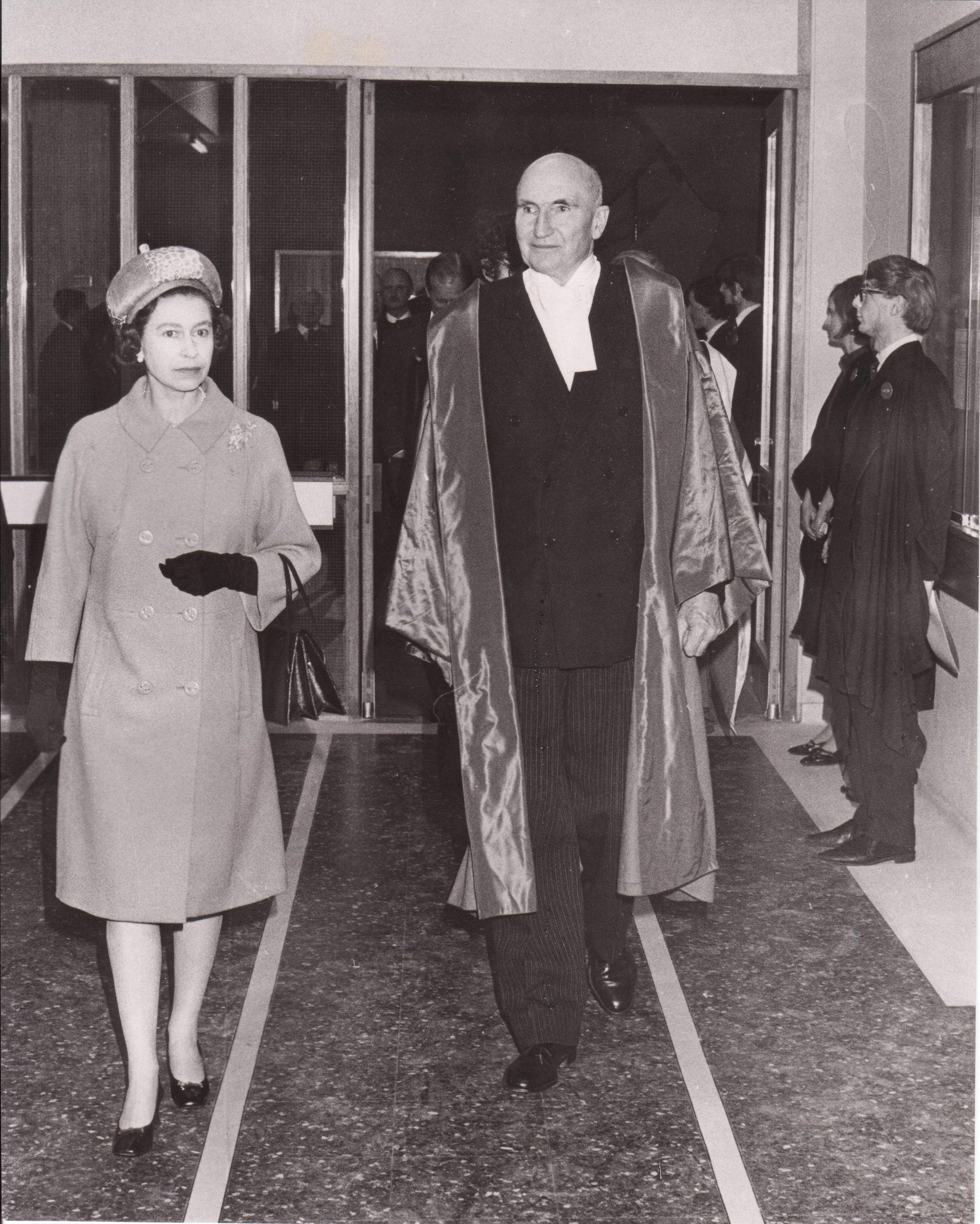 An archive black and white photograph of Queen Elizabeth II walking into the College Block with Lord Sherfield.
