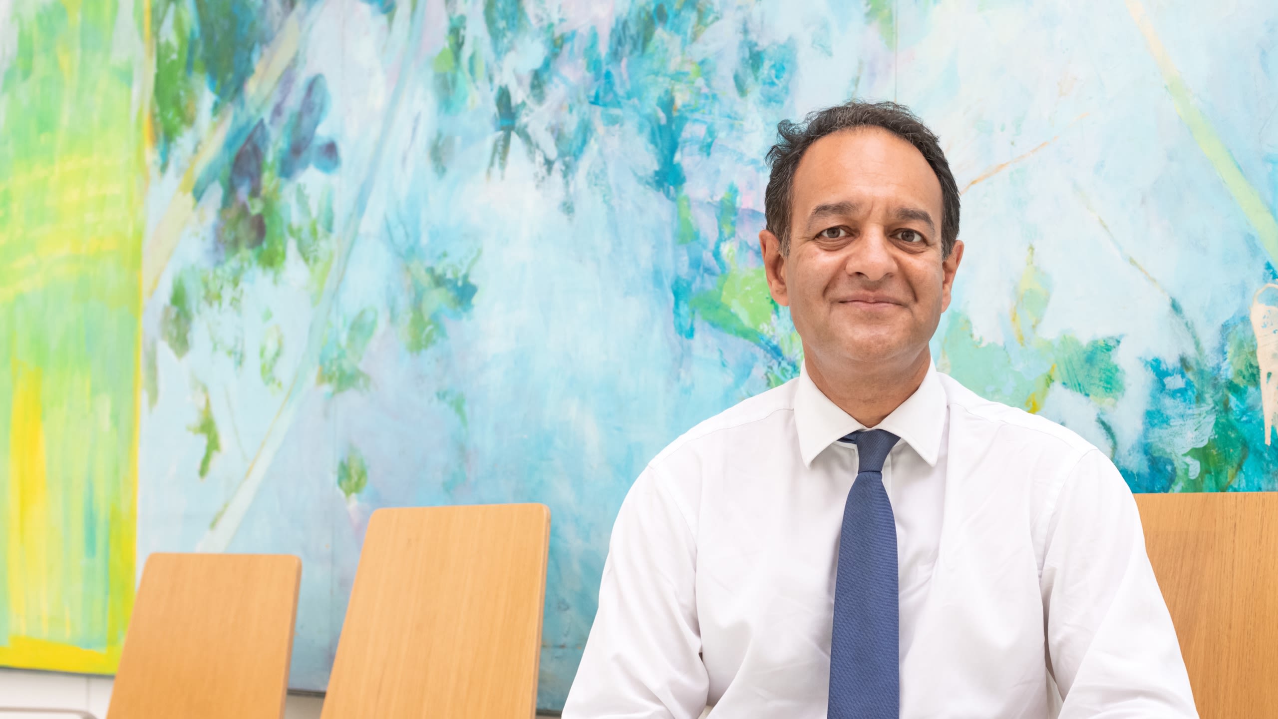 Professor Suveer Singh sitting infront of blue and green painting at Chelsea and Westminster Hospital
