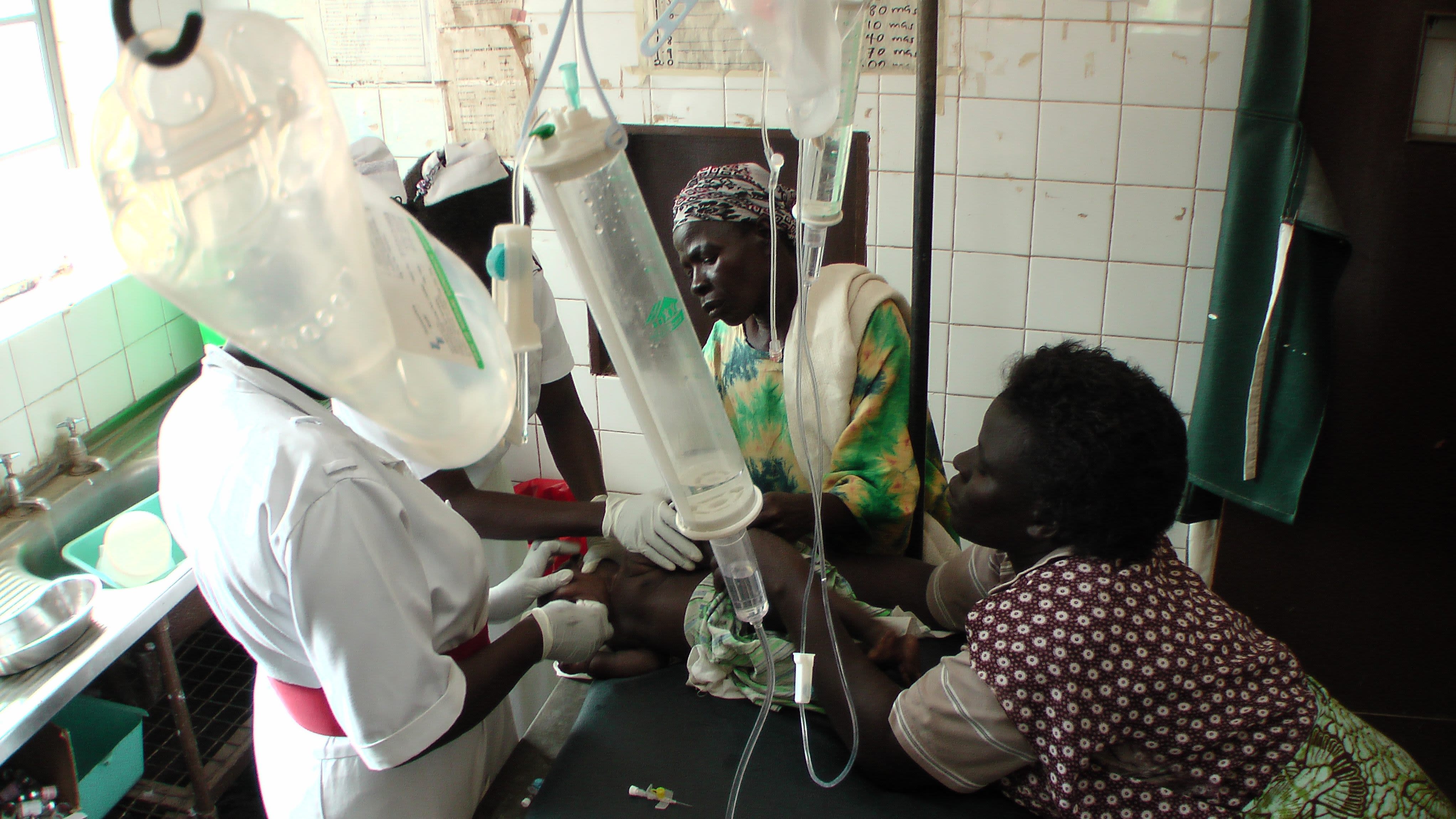 A child (lying) receiving IV fluids from three healthcare workers