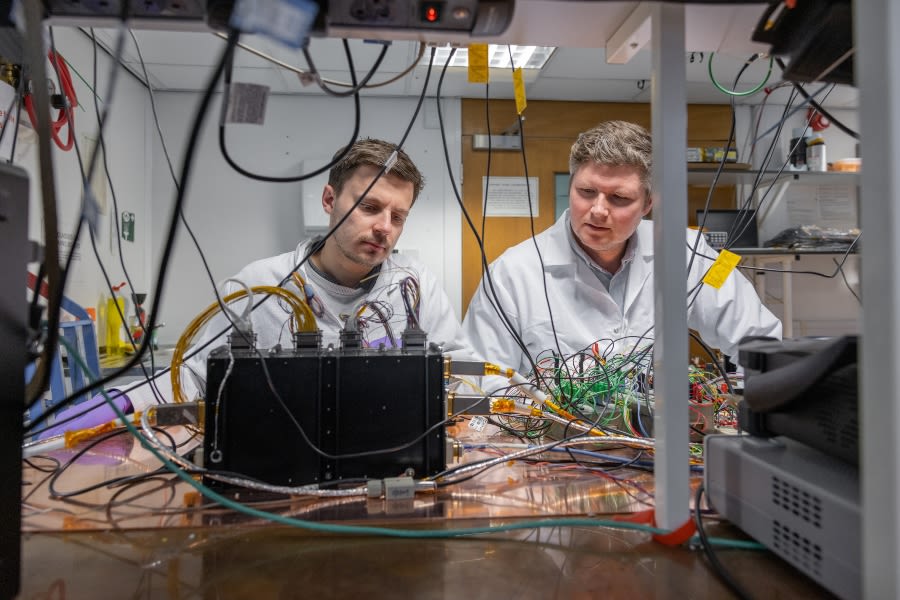 Two men in white coats look at a tangle of wires and a black box