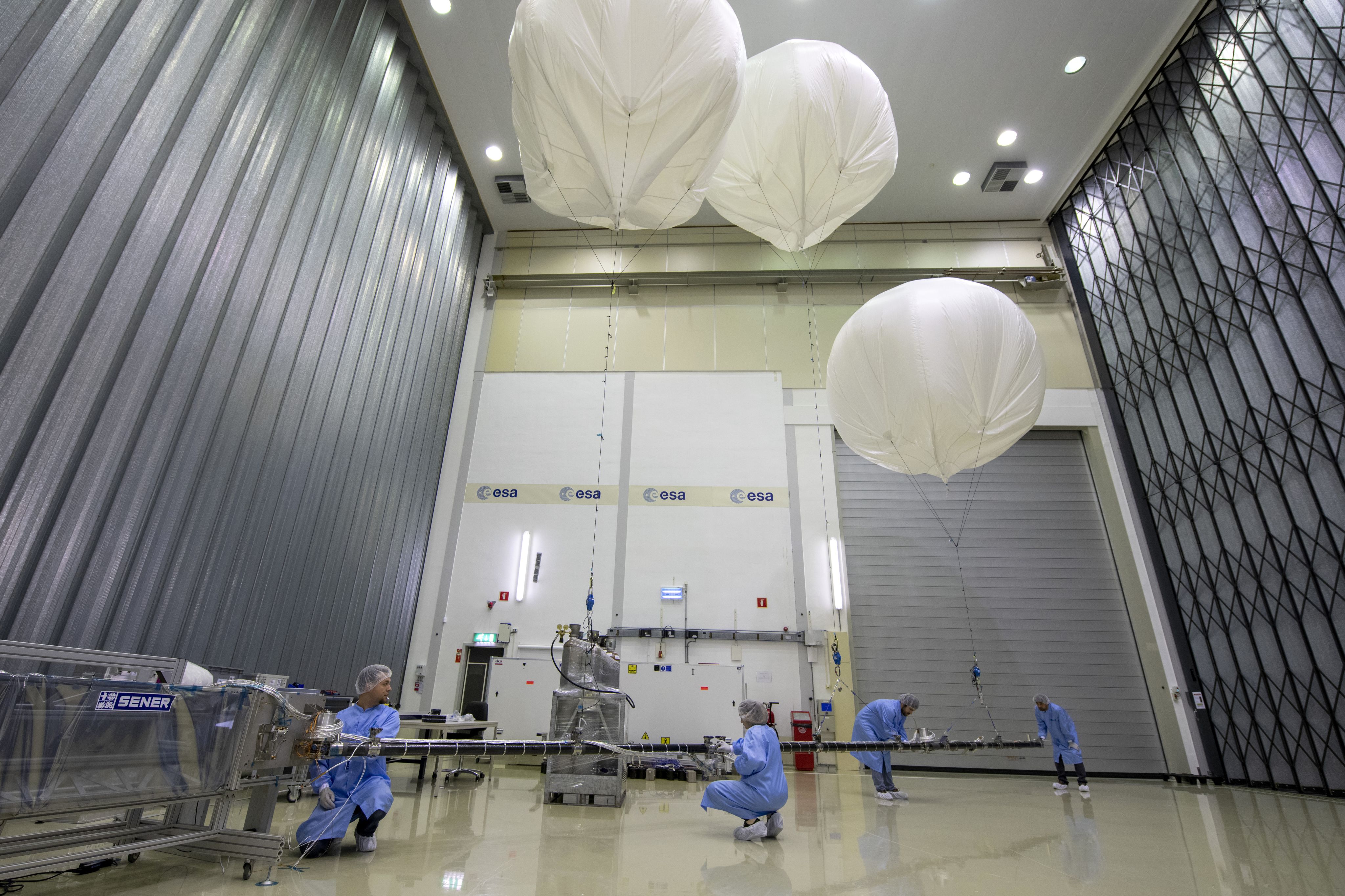 People in blue clean suits unfolding a long boom held up by three large balloons