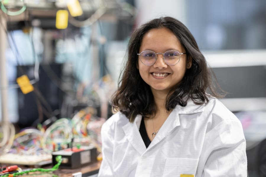 A woman wearing glasses and a white coat smiles at the camera