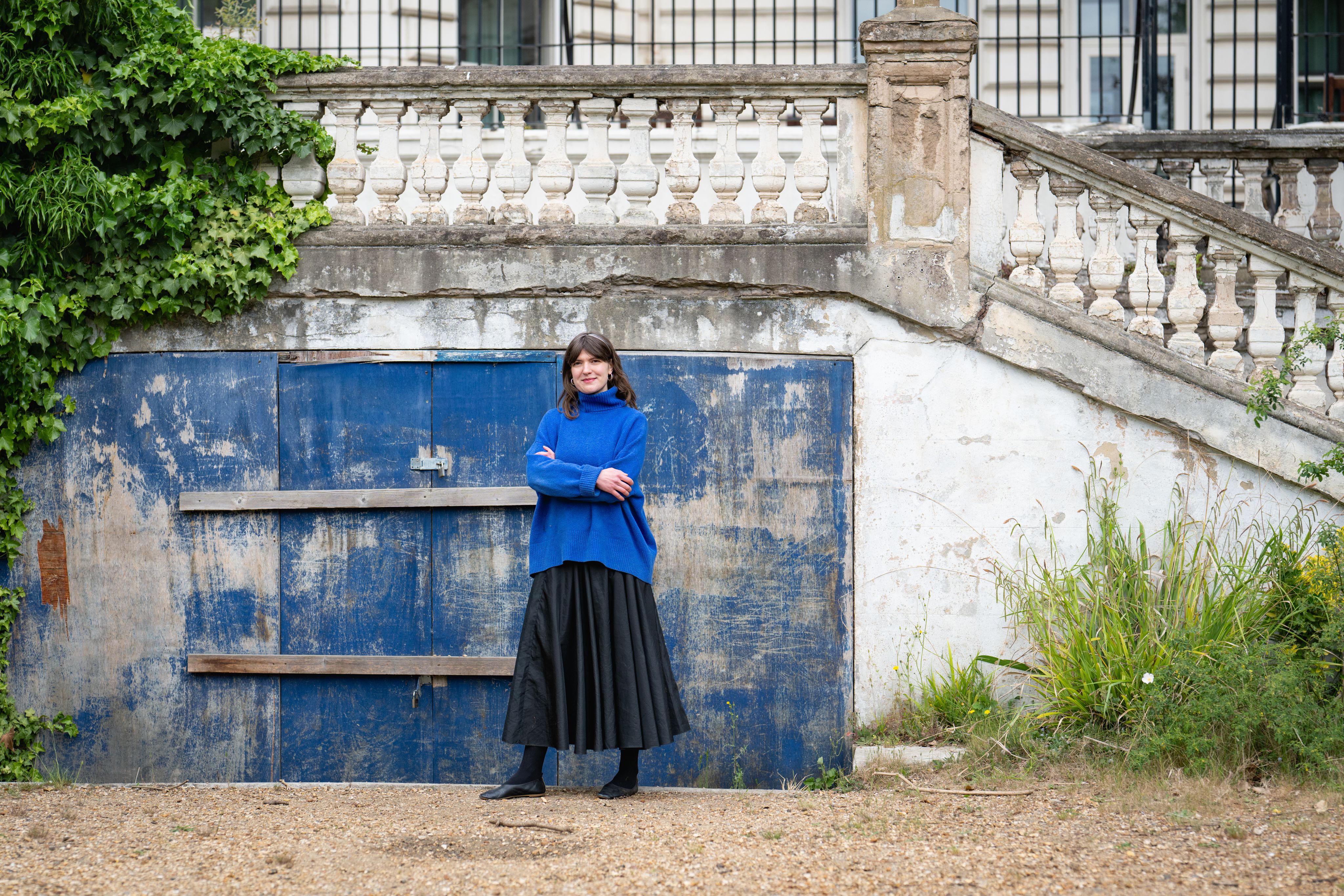 Liva standing with her arms crossed in front of a rustic blue door outside.