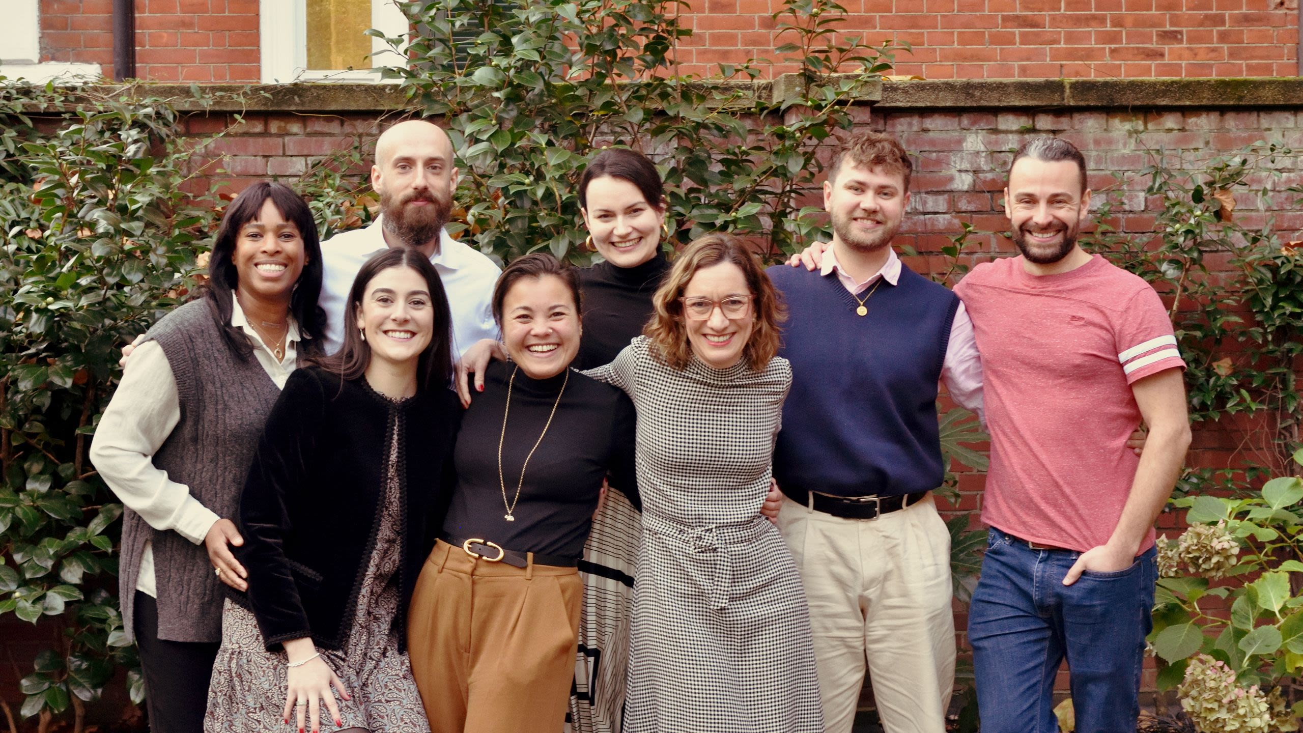 group of 8 people, standing, hugging, and smiling at the camera