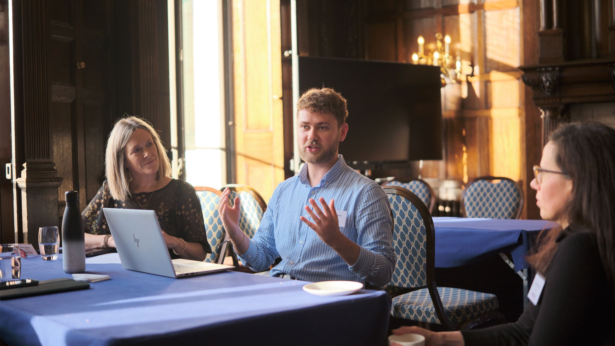 person with laptop gesturing and talking to 2 other people