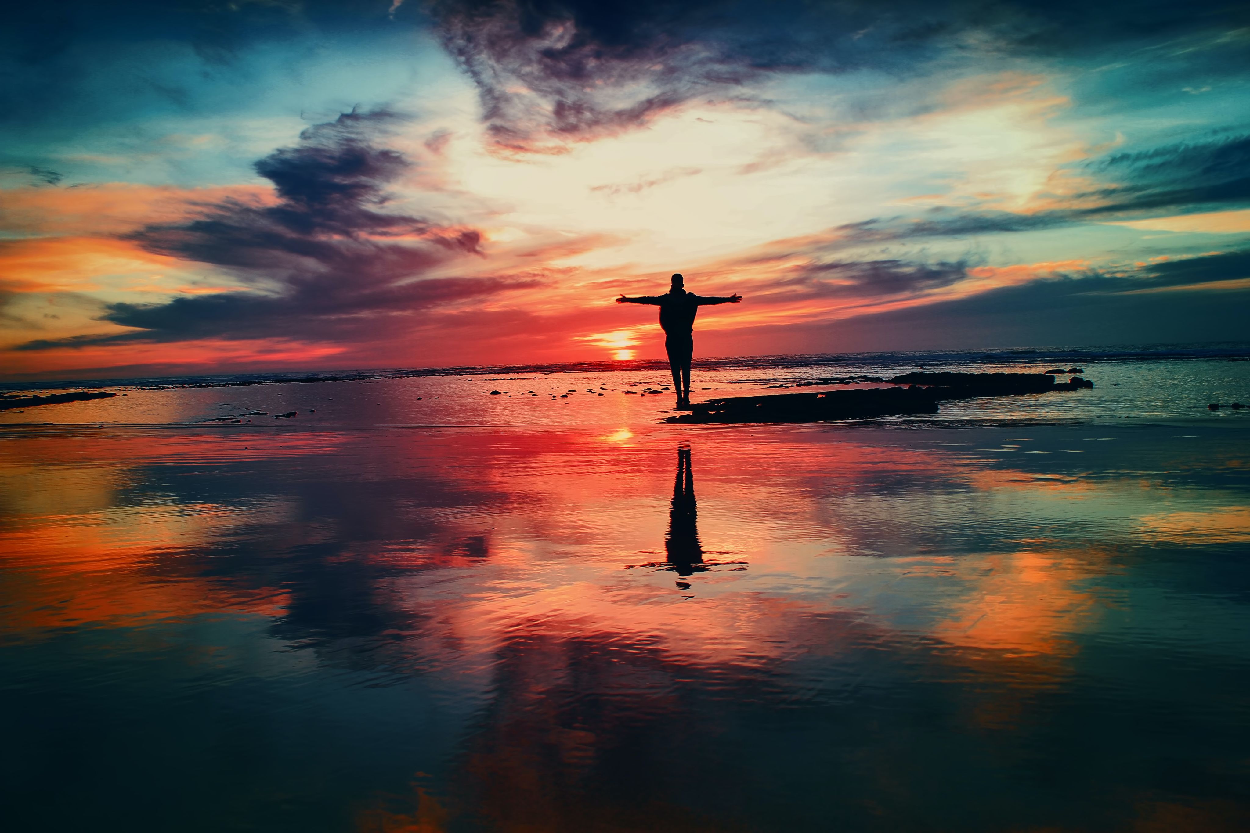 Person on beach in front of sunset. Photo by Mohamed Nohassi on Unsplash