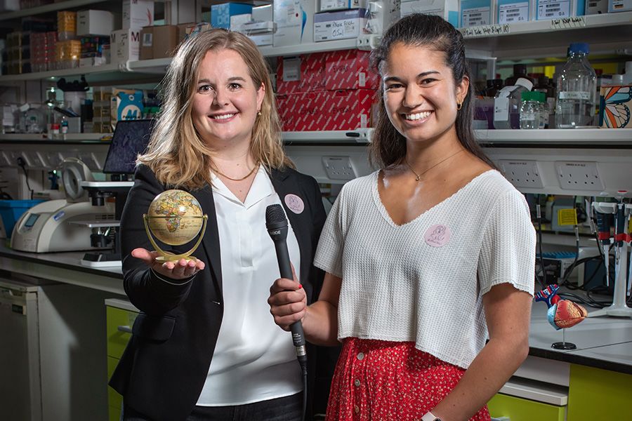 Maike and Salina hold a globe and microphone in a lab