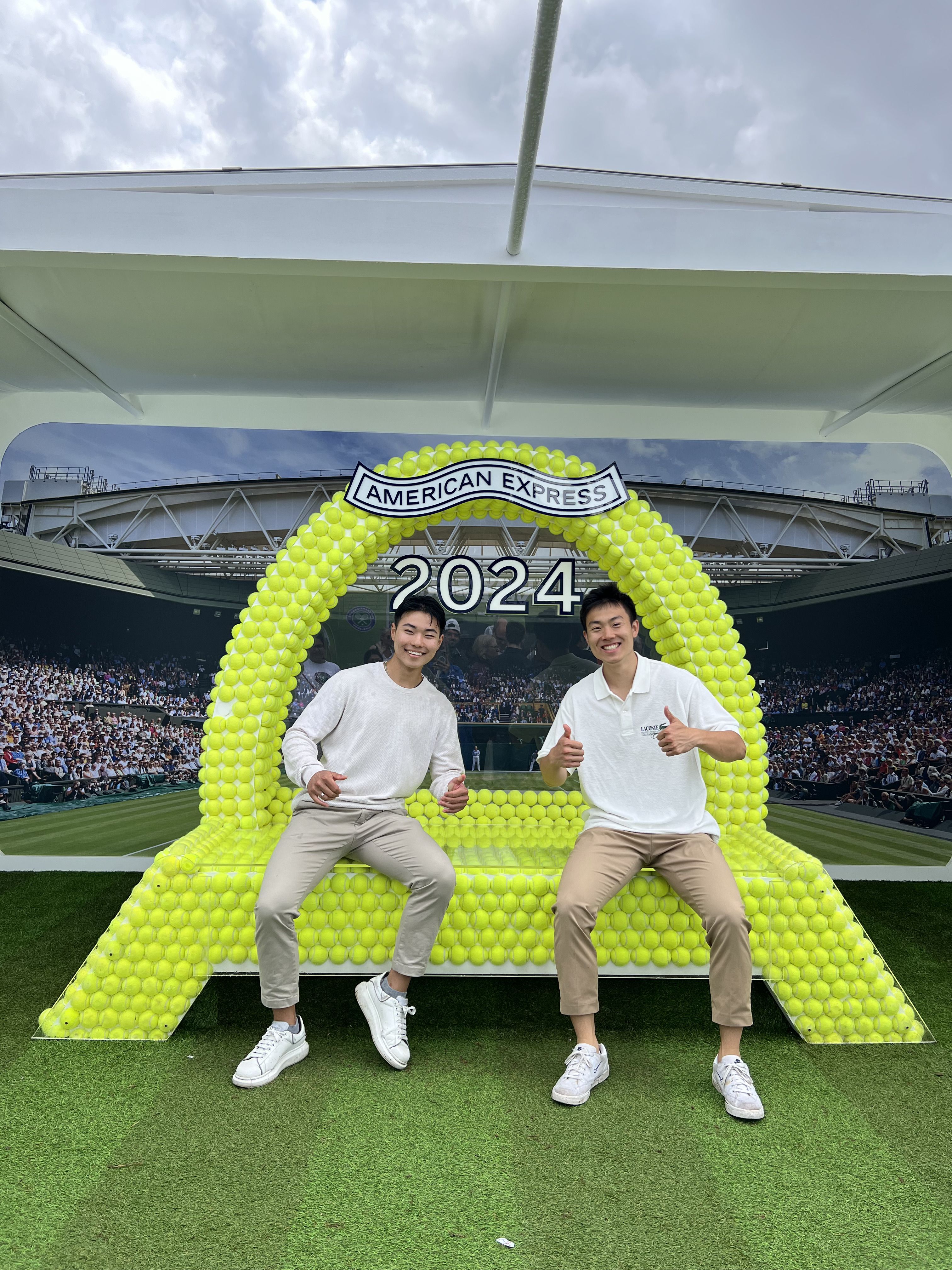 Andrew and a friend sitting on a bench made of tennis balls at Wimbledon 2024.