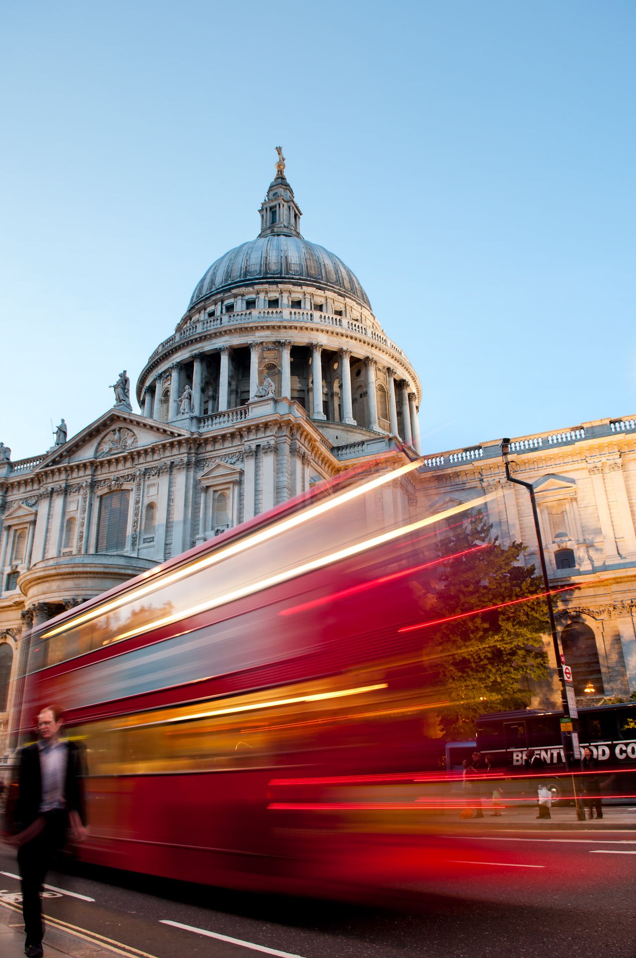 A red London bus drives past St Paul's Cathedral in a blur