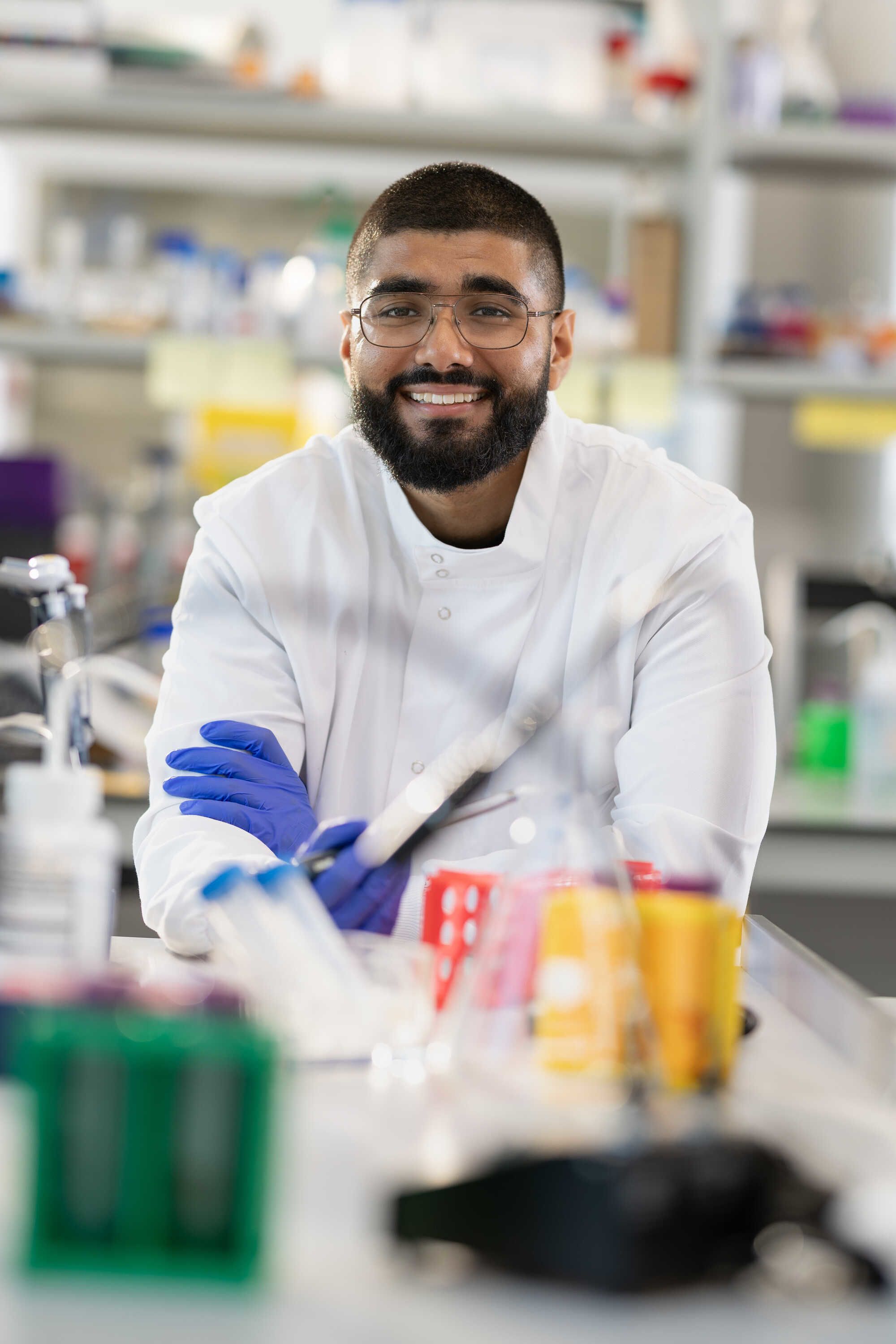Haaris in a lab, wearing a white lab coat and lab gloves