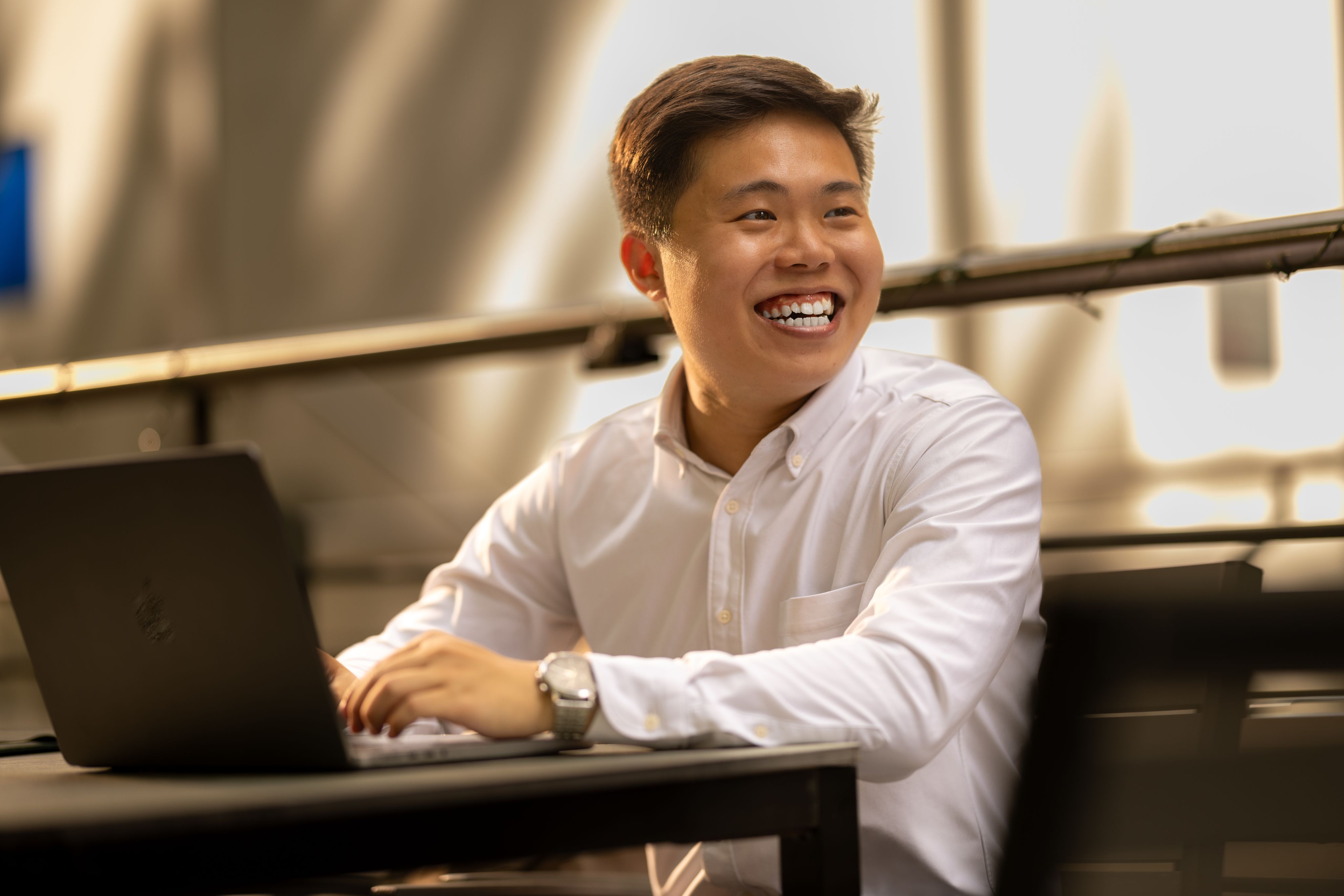 Han Ming sitting down on his laptop and smiling looking off camera