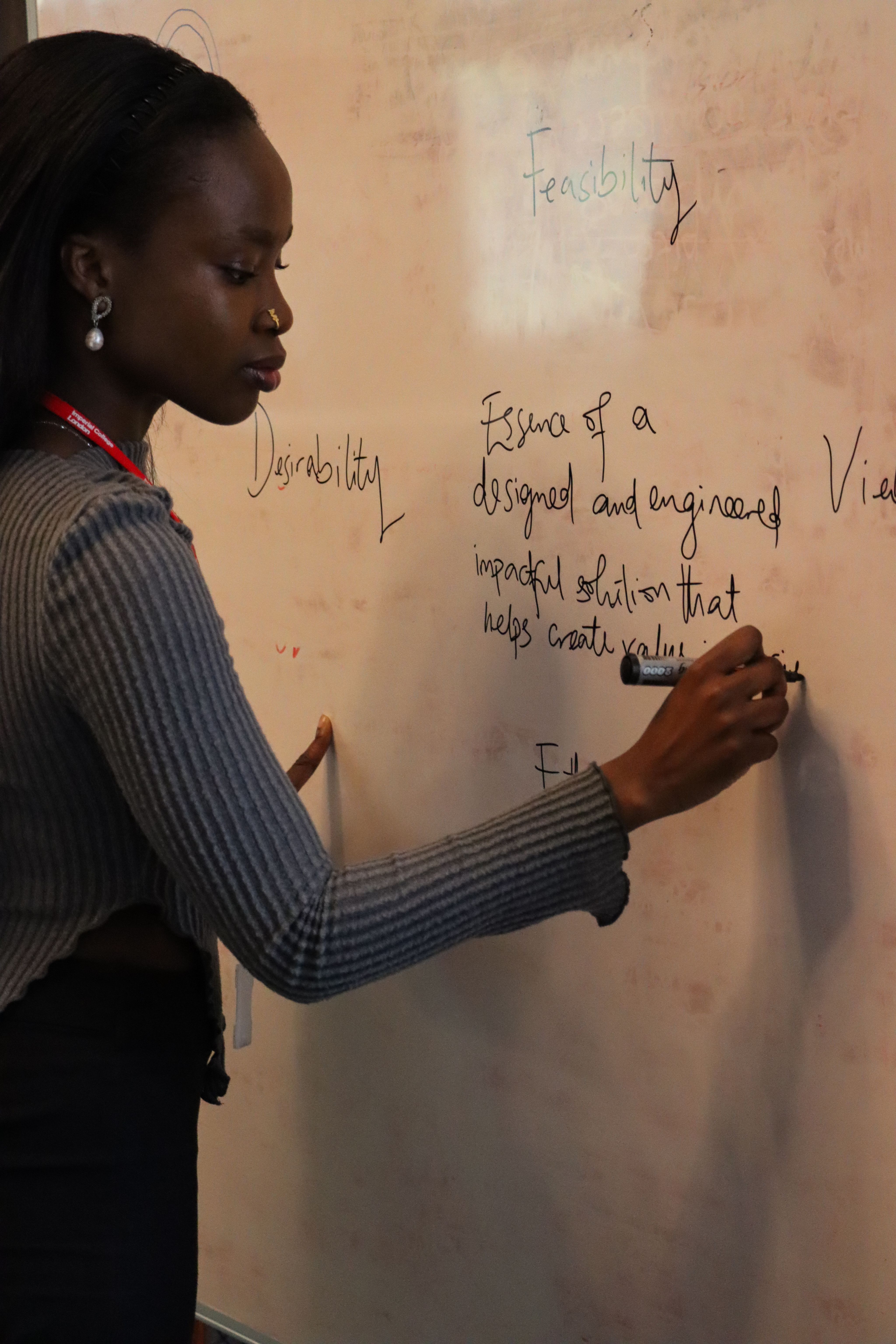 Ifeoluwa writing on a whiteboard, including "Essence of a designed and engineered impactful solution that helps create..."