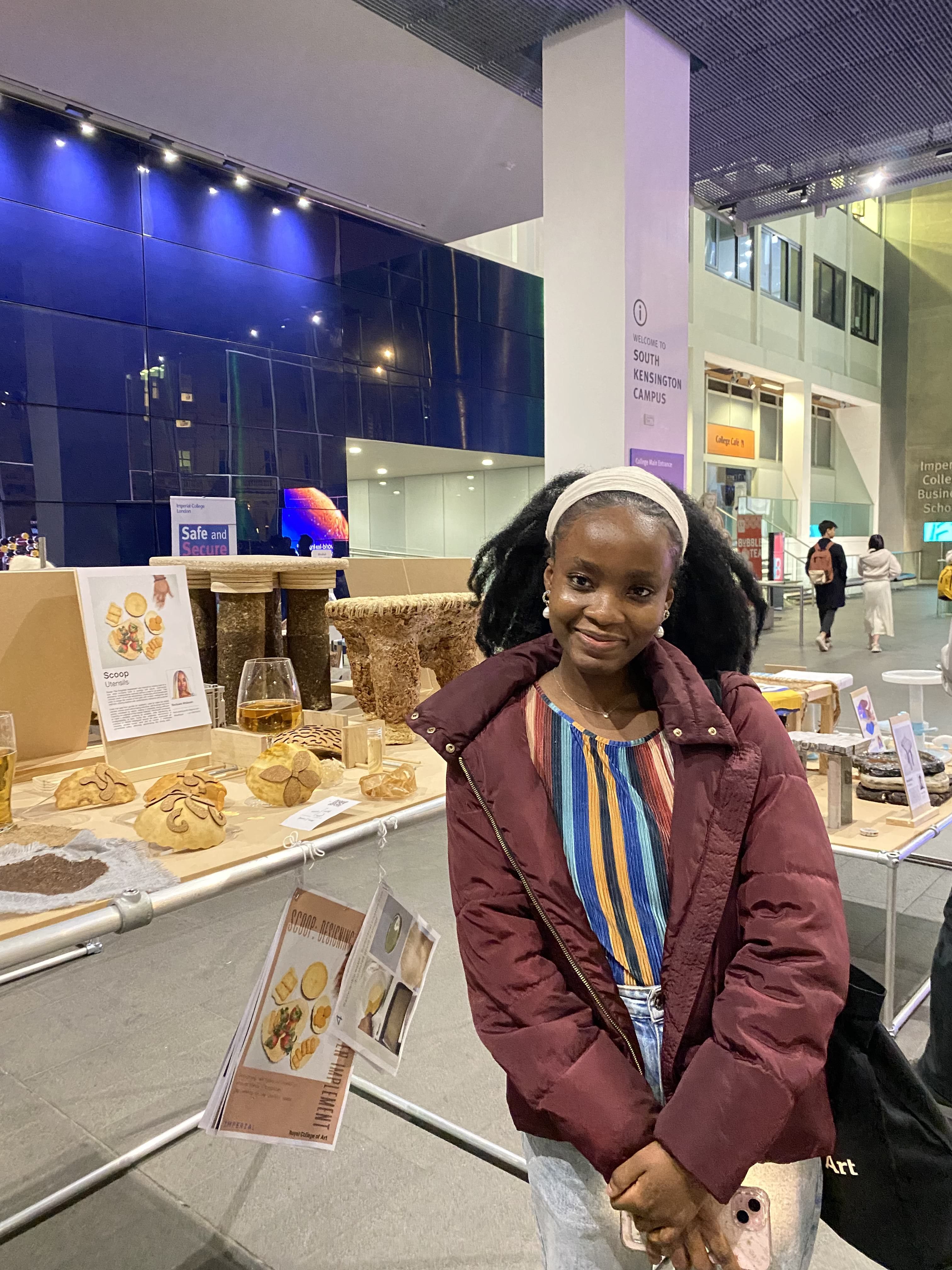 Ifeoluwa standing in front of a showcase of design work in the main entrance to Imperial College London