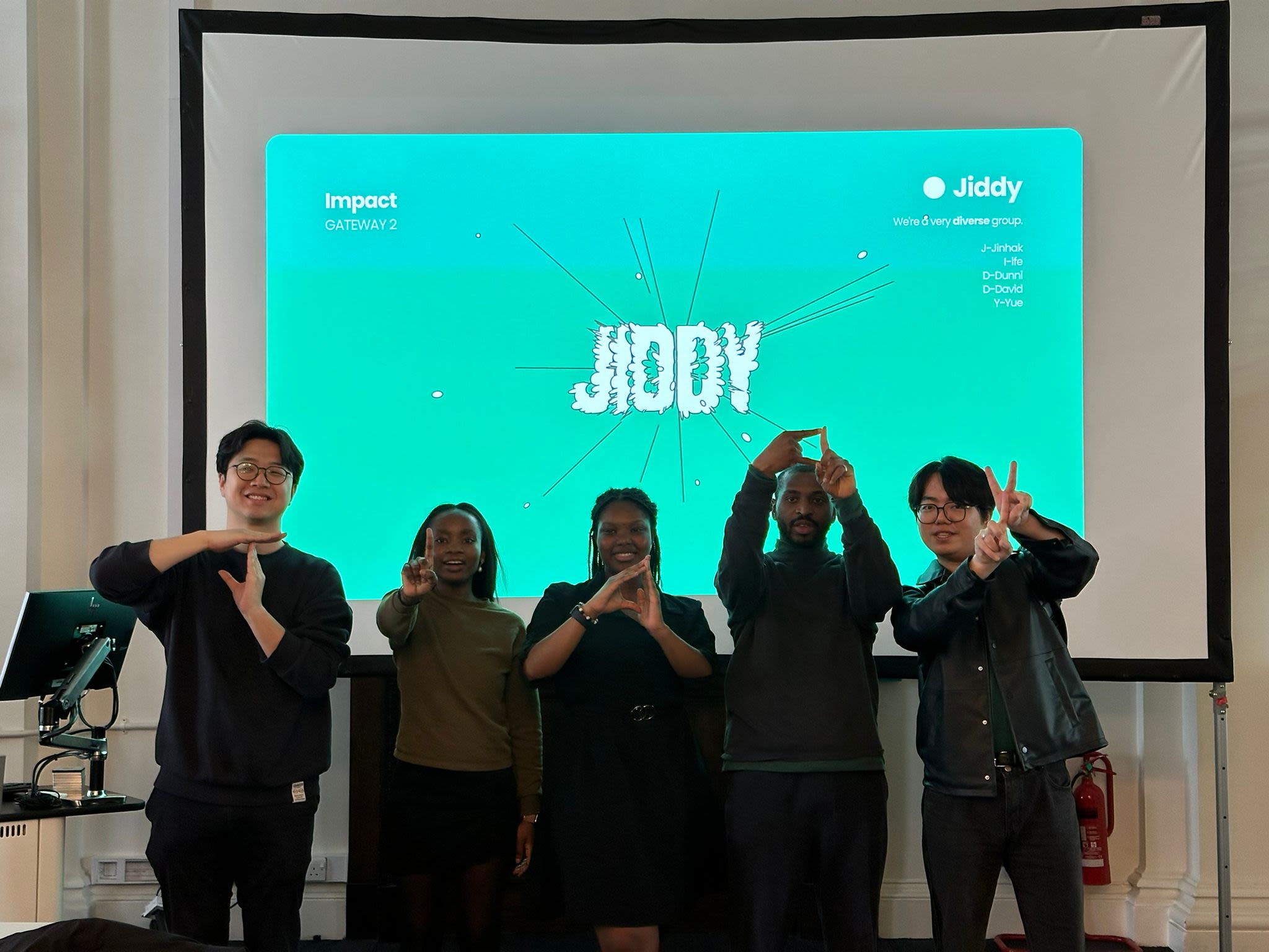 Ifeoluwa posing with one of her group project teams in front of a projector screen showing their team logo