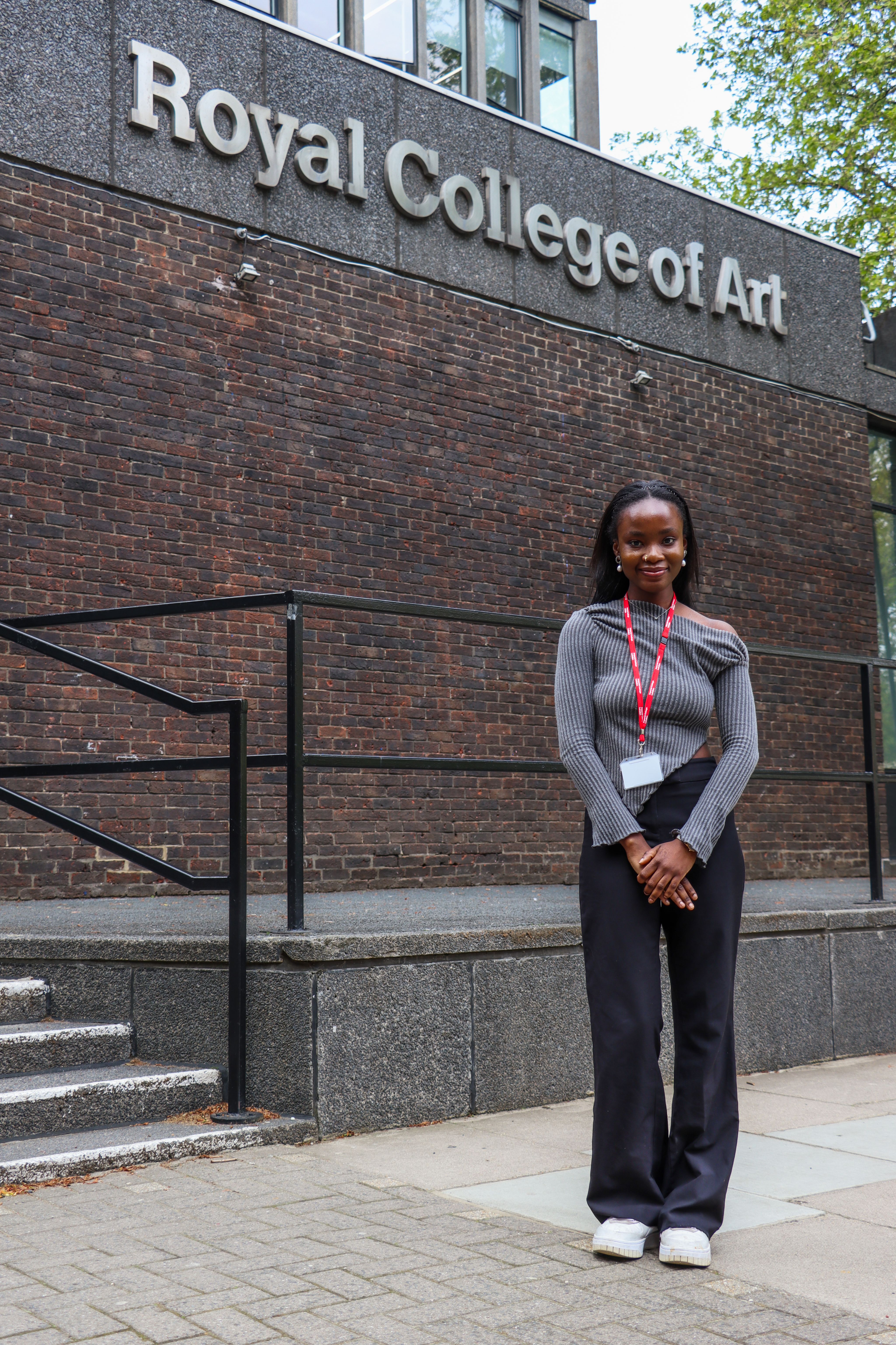 Ifeoluwa standing outdoors in front of the Royal College of Art with 'Royal College of Art' signage in the background