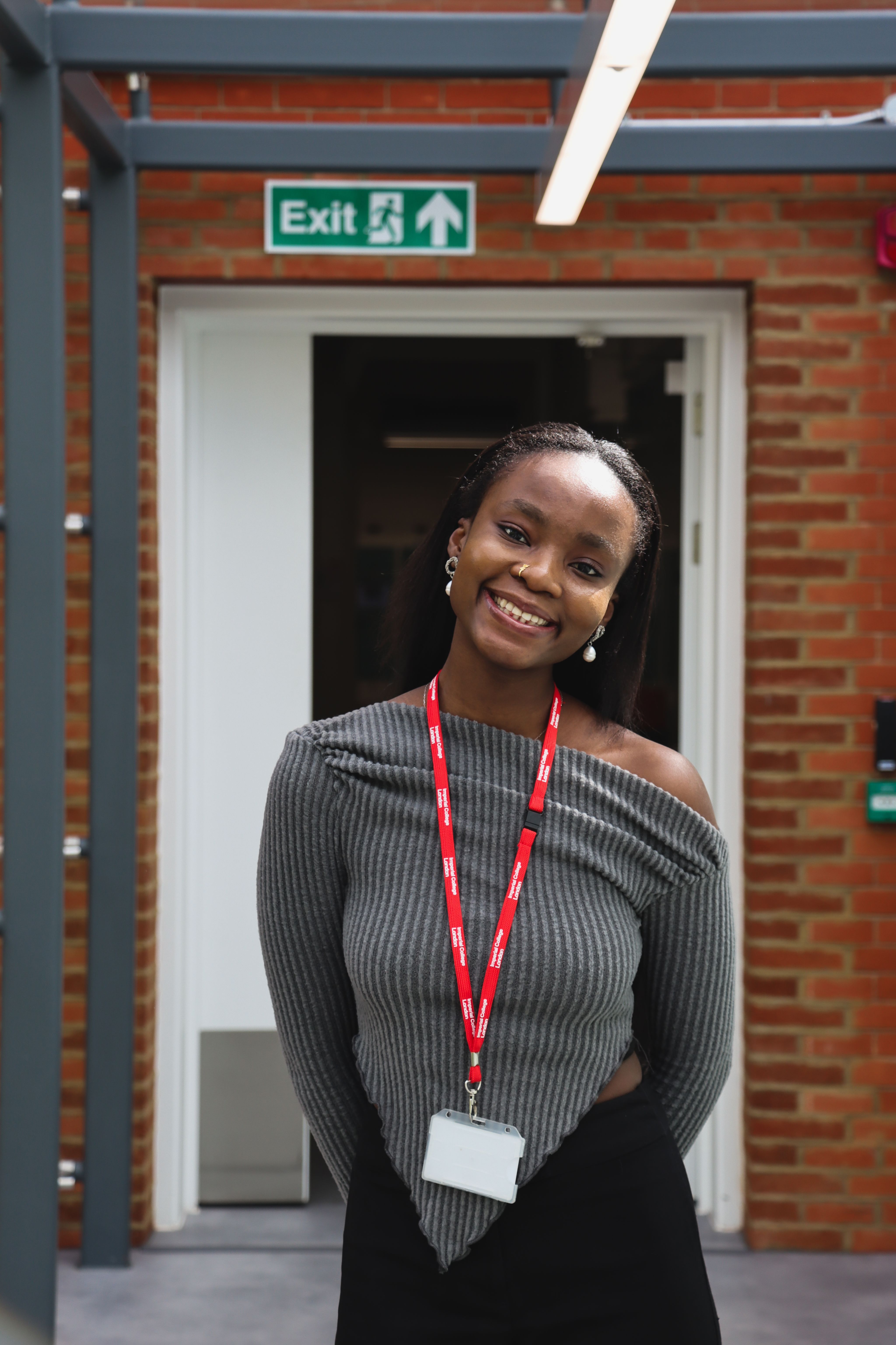 Ifeoluwa smiling and looking directly at the camera in front of a brick background